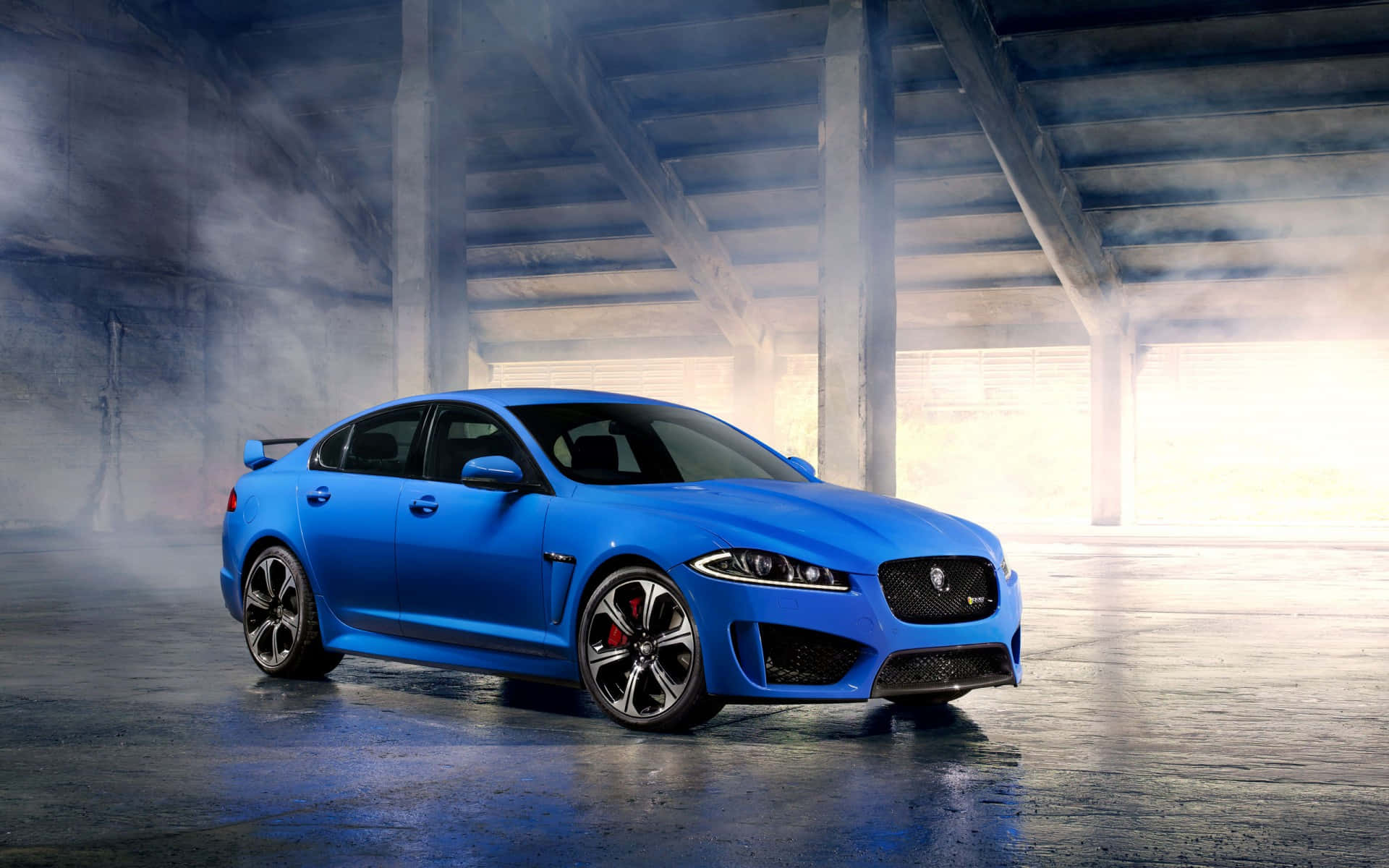 Jaguar Xfr 桌布 壁紙 — 一輛充滿活力的藍色積架跑車在霧氣瀰漫的混凝土地下通道中，在工業橫樑下戲劇性的燈光下閃閃發光。