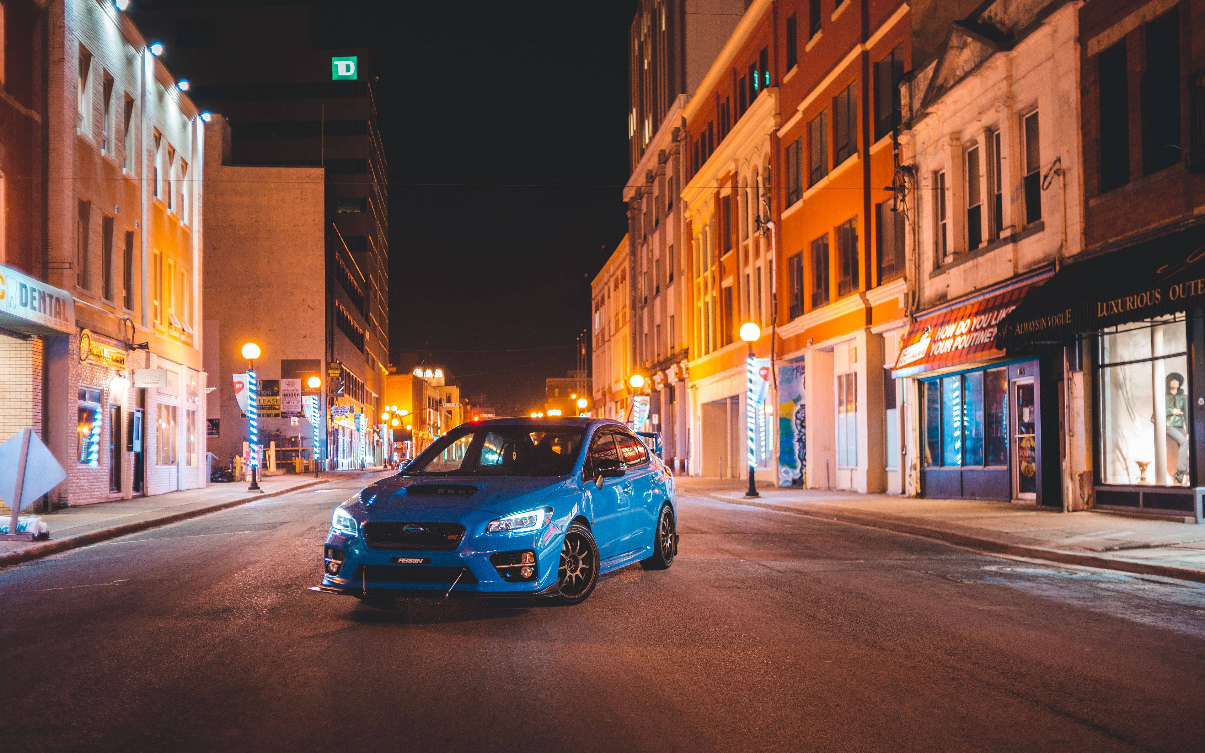 subaru 桌布 壁紙 — 一輛充滿活力的藍色跑車在夜間寧靜的城市街道上，在溫暖的路燈下閃耀。