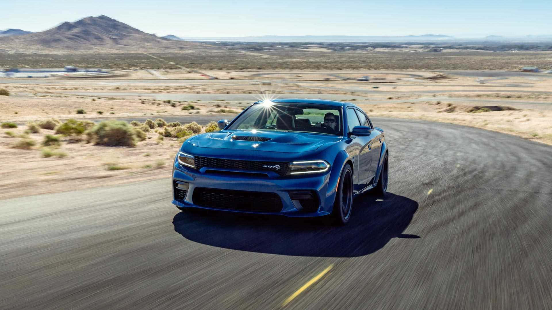 Dodge Charger 桌布 壁紙 — 一輛充滿活力的藍色道奇Charger Daytona在明亮的日光下沿著沙漠公路飛馳，背景是遠處的山脈。
