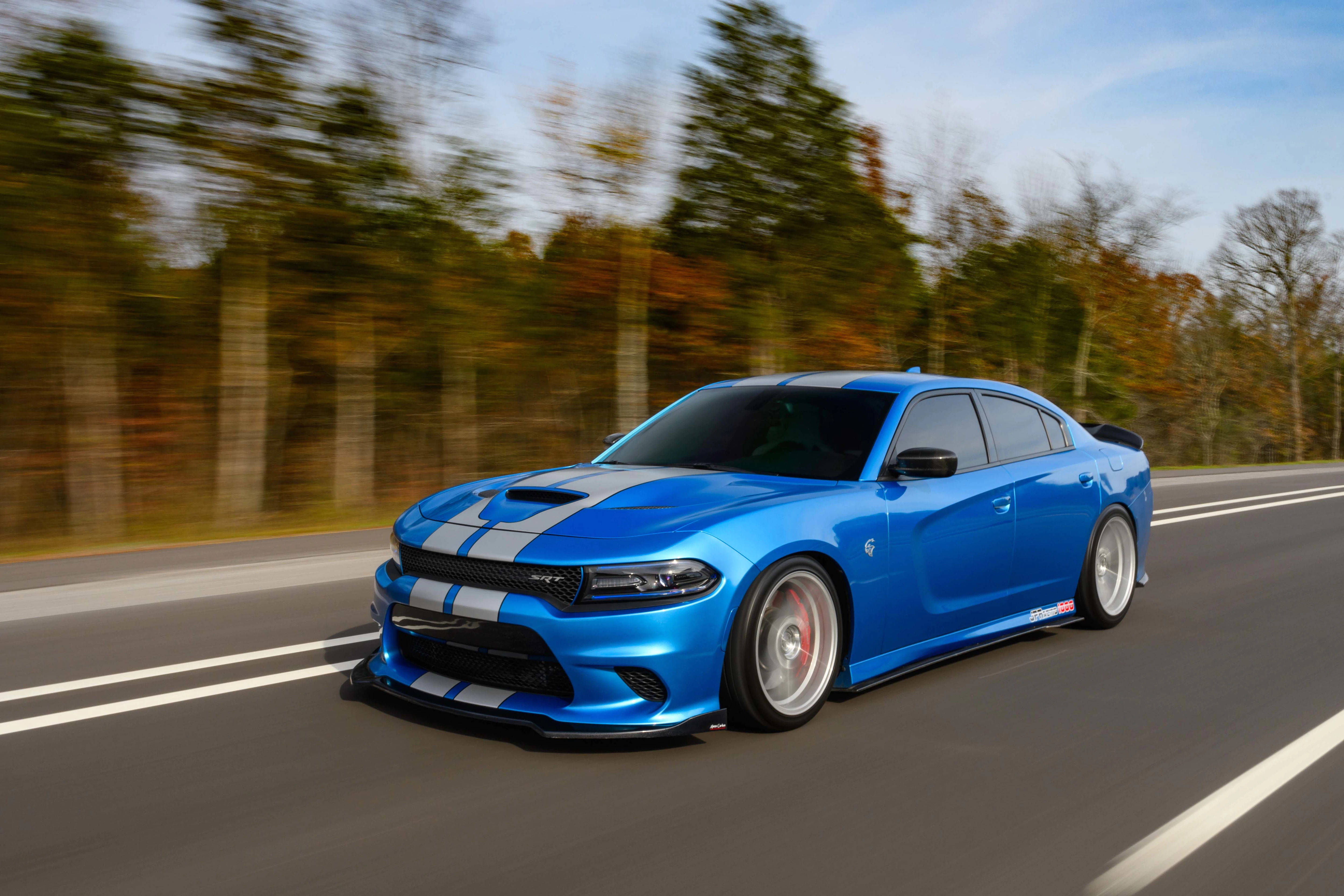 Mopar 2016 Dodge Charger SRT 392 壁紙 — 一輛充滿活力的藍色道奇Charger，帶有白色賽車條紋，在晴朗的天空下，沿著兩旁秋樹的道路飛馳。