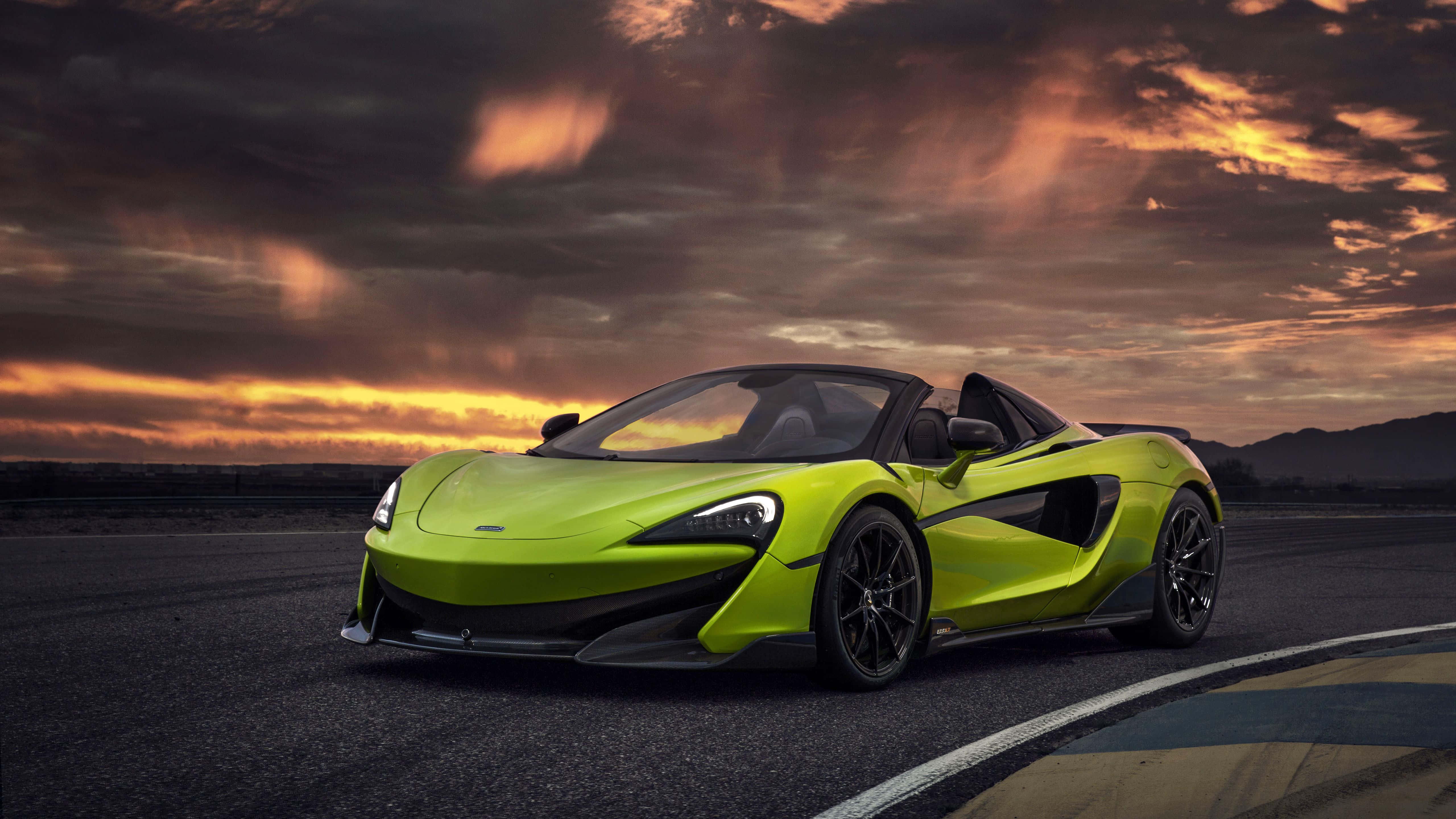 麥拿侖 桌布 壁紙 — 一輛充滿活力的青檸綠色McLaren跑車停泊在賽道上，背景是壯麗的日落天空，帶有火紅橙色的雲彩。