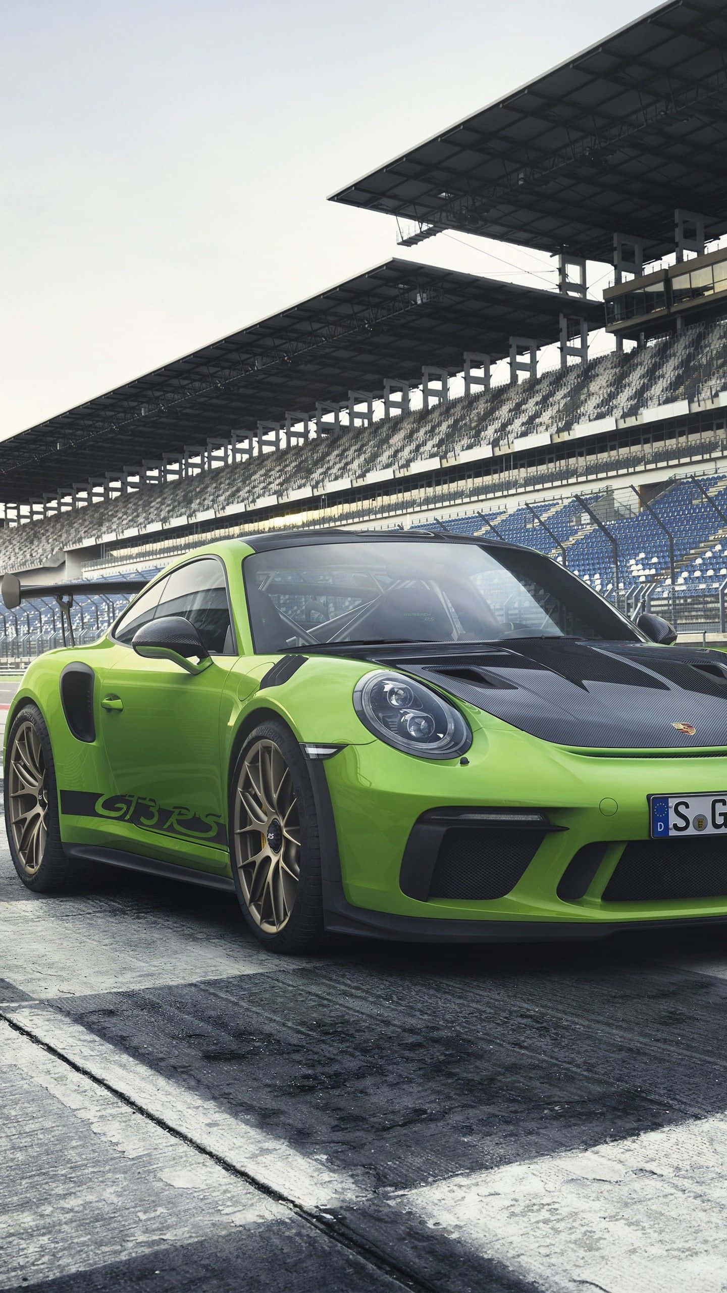 Porsche iPhone 桌布 壁紙 — 一輛充滿活力的青檸綠色保時捷 911 GT3 RS 停在潮濕的賽道上，天空陰沉，身後是空無一人的看台。