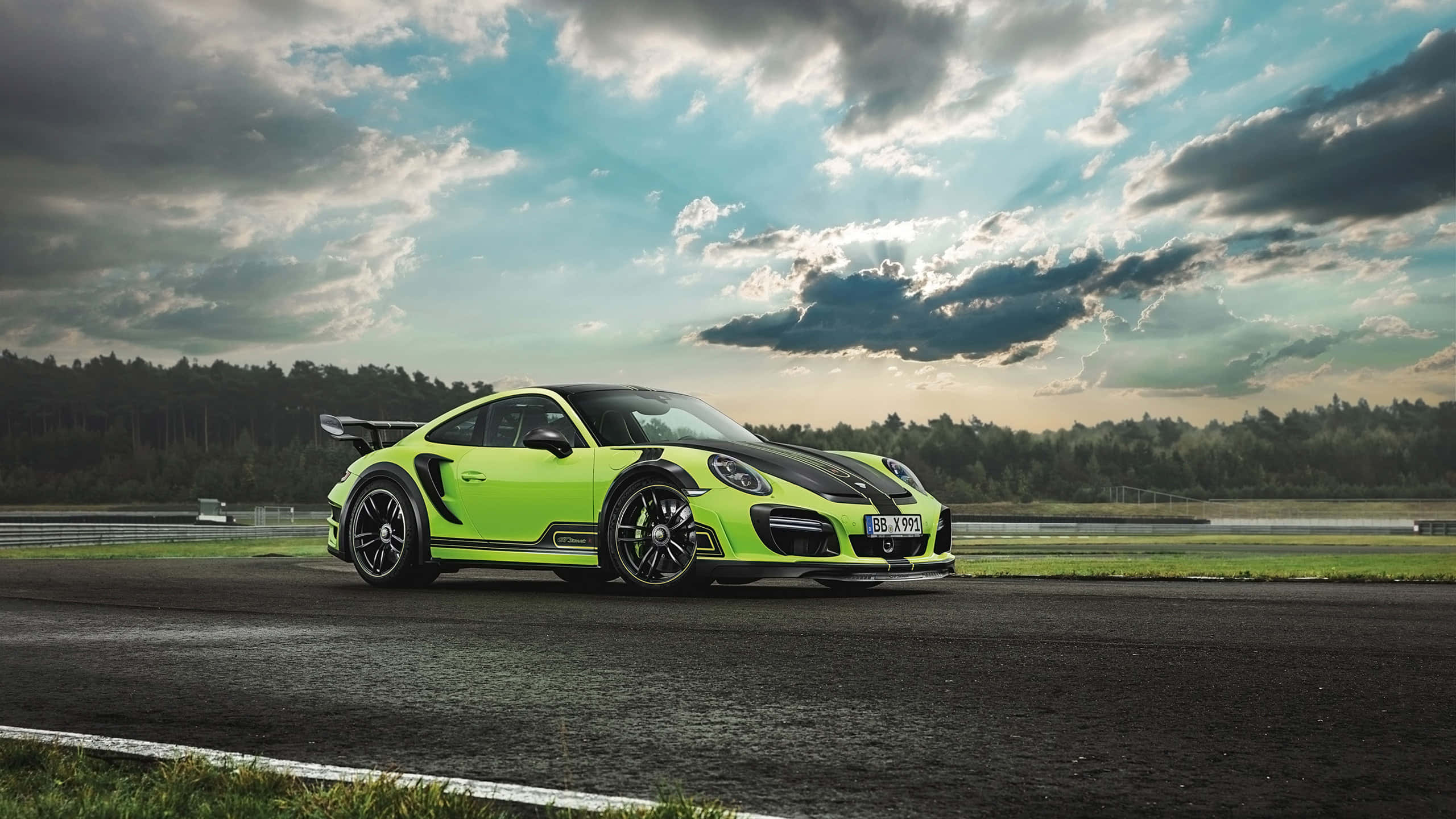 保時捷 桌布 壁紙 — 一輛充滿活力的青檸綠色保時捷911 GT2 RS，帶有黑色點綴，在戲劇性的多雲天空下，停在潮濕的賽道上。