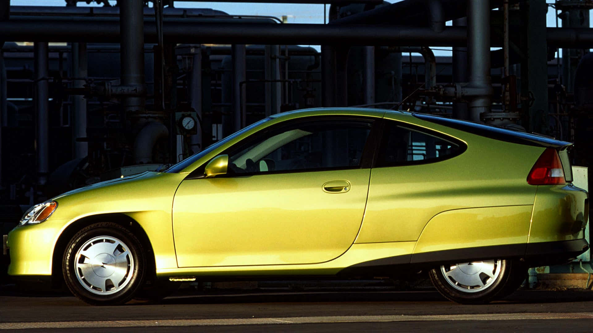Honda Insight 桌布 壁紙 — 一輛充滿活力的青檸綠色混合動力跑車在明亮的日光下停放在工業管道旁邊。