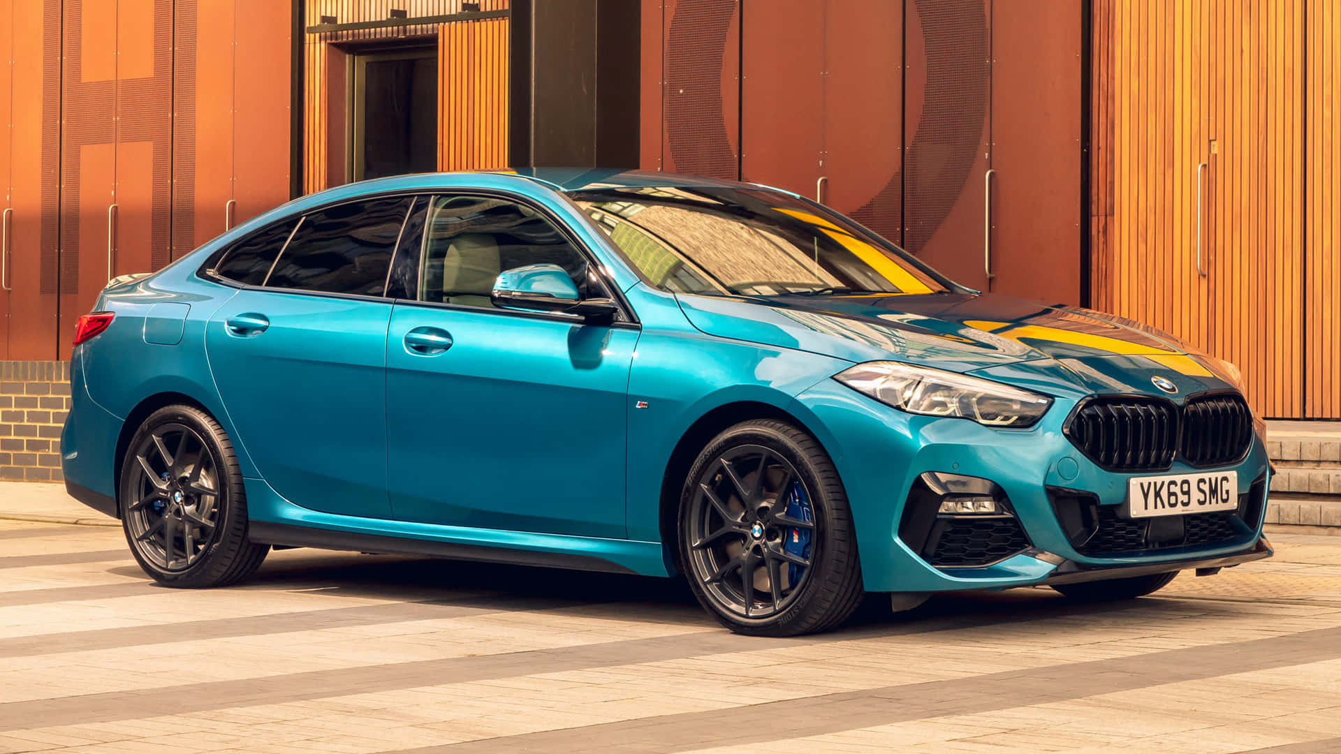 Bmw 2 Series 桌布 壁紙 — 一輛充滿活力的青綠色BMW M240i停泊在瓷磚廣場上，背景是暖色調的木質建築外牆。