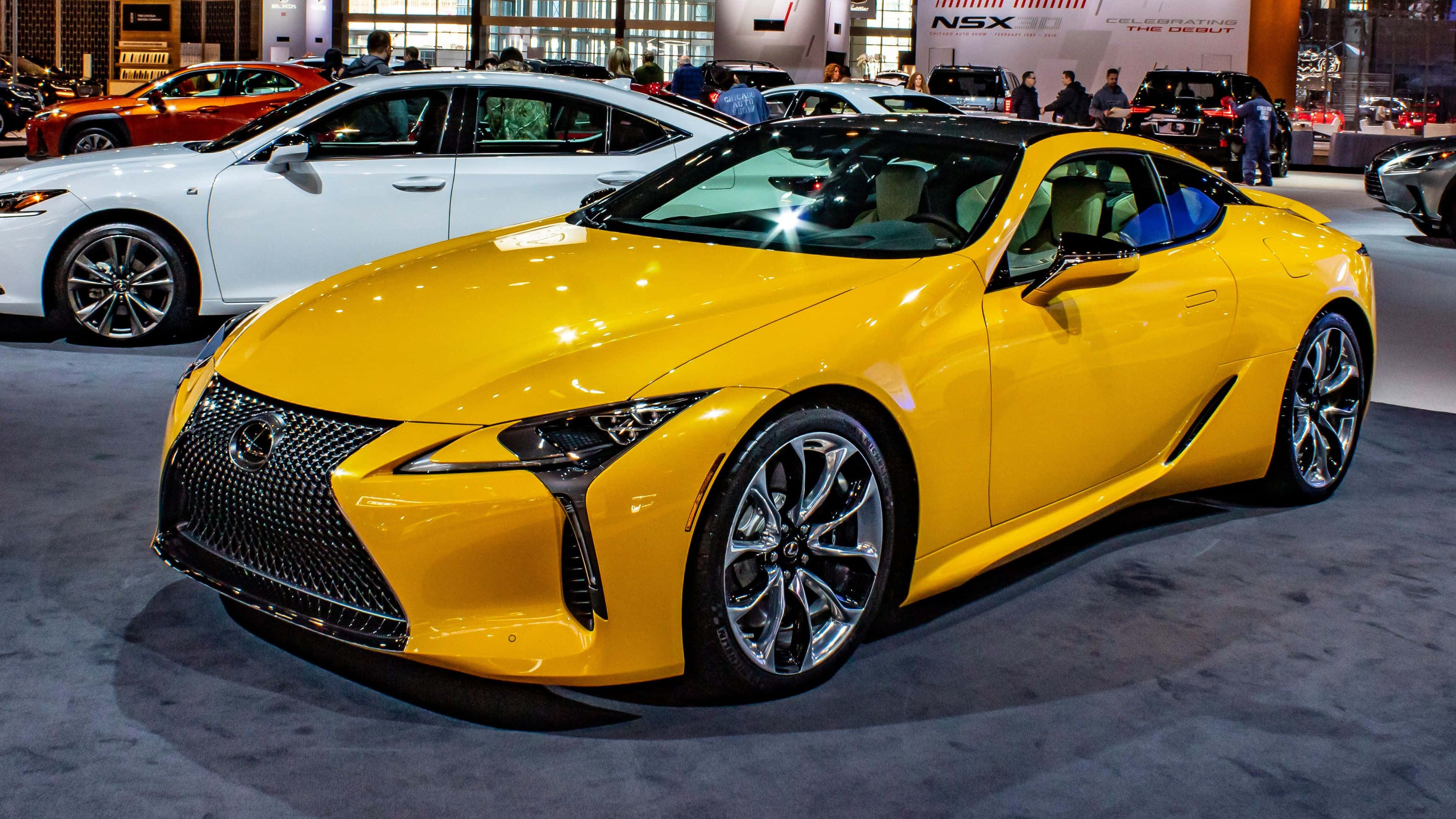 Yellow Car 桌布 壁紙 — 一輛充滿活力的黃色Lexus跑車在室內車展的明亮燈光下閃閃發光，背景有其他車輛。