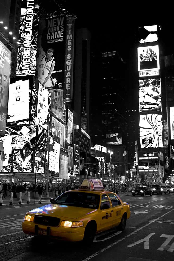 Yellow Cab 桌布 壁紙 — 一輛充滿活力的黃色出租車在夜晚穿梭於紐約市繁忙的街道，周圍環繞著高聳的燈光廣告牌和人群。