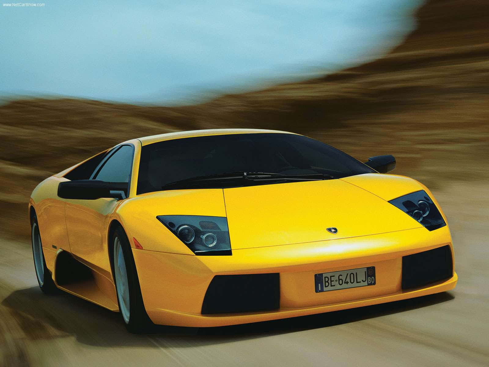 Lamborghini Murciélago 桌布 壁紙 — 一輛充滿活力的黃色林寶堅尼 Murciélago 在沙漠景觀中疾馳，動態模糊強調了其力量和流線型設計。