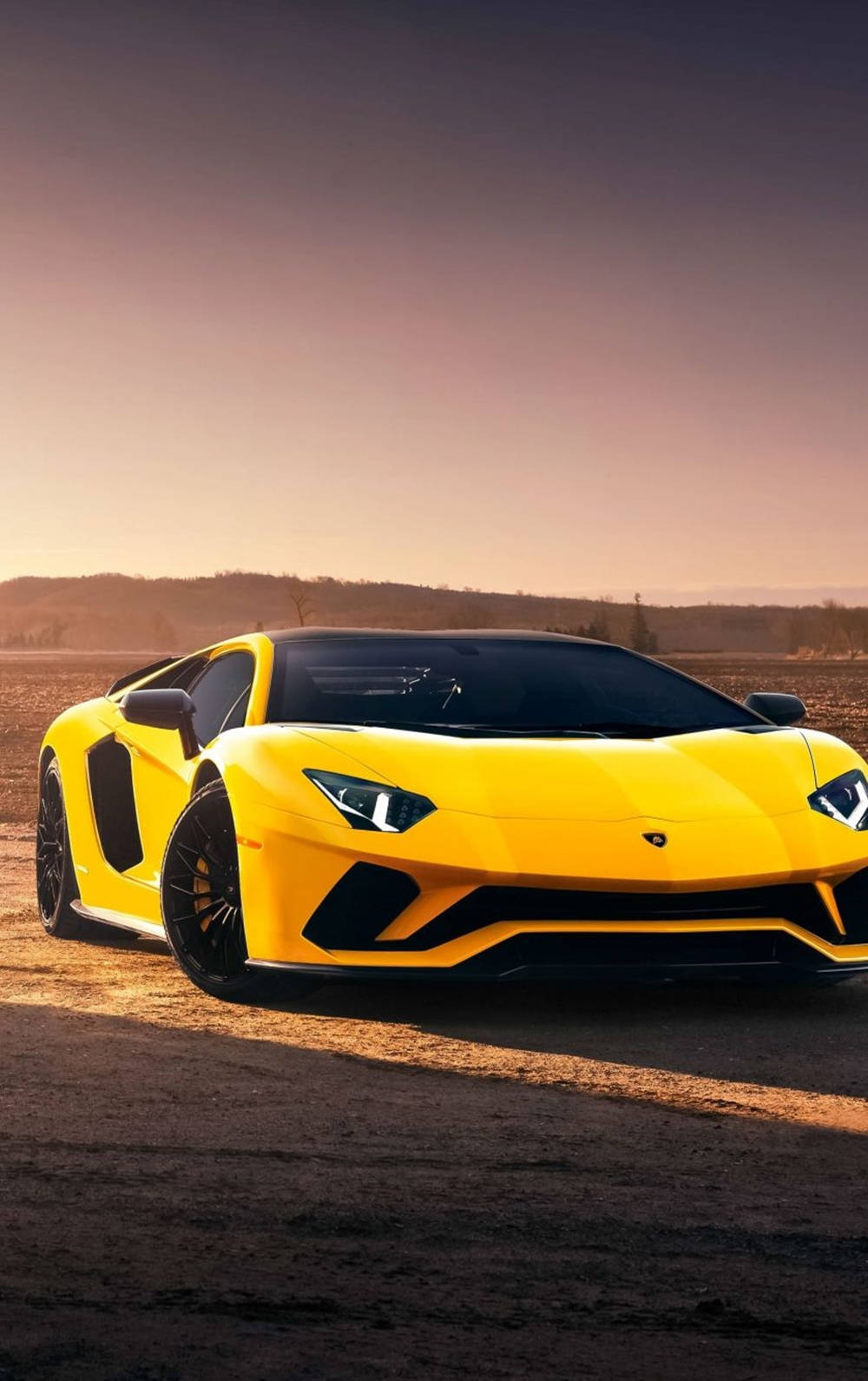 Sports Car 桌布 壁紙 — 一輛充滿活力的黃色林寶堅尼Aventador在日落時分停在塵土飛揚的道路上，溫暖的金色光芒投下長長的影子。