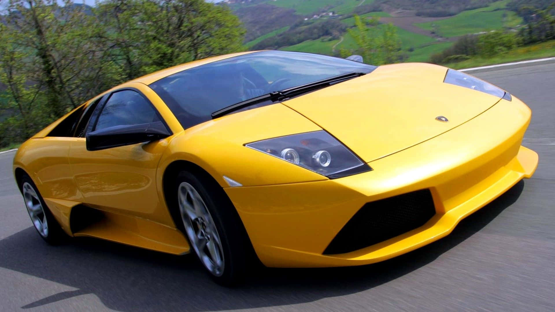 Lamborghini Murciélago 桌布 壁紙 — 一輛充滿活力的黃色林寶堅尼Gallardo在蜿蜒的山路上疾馳，背景是鬱鬱蔥蔥的綠色山丘。