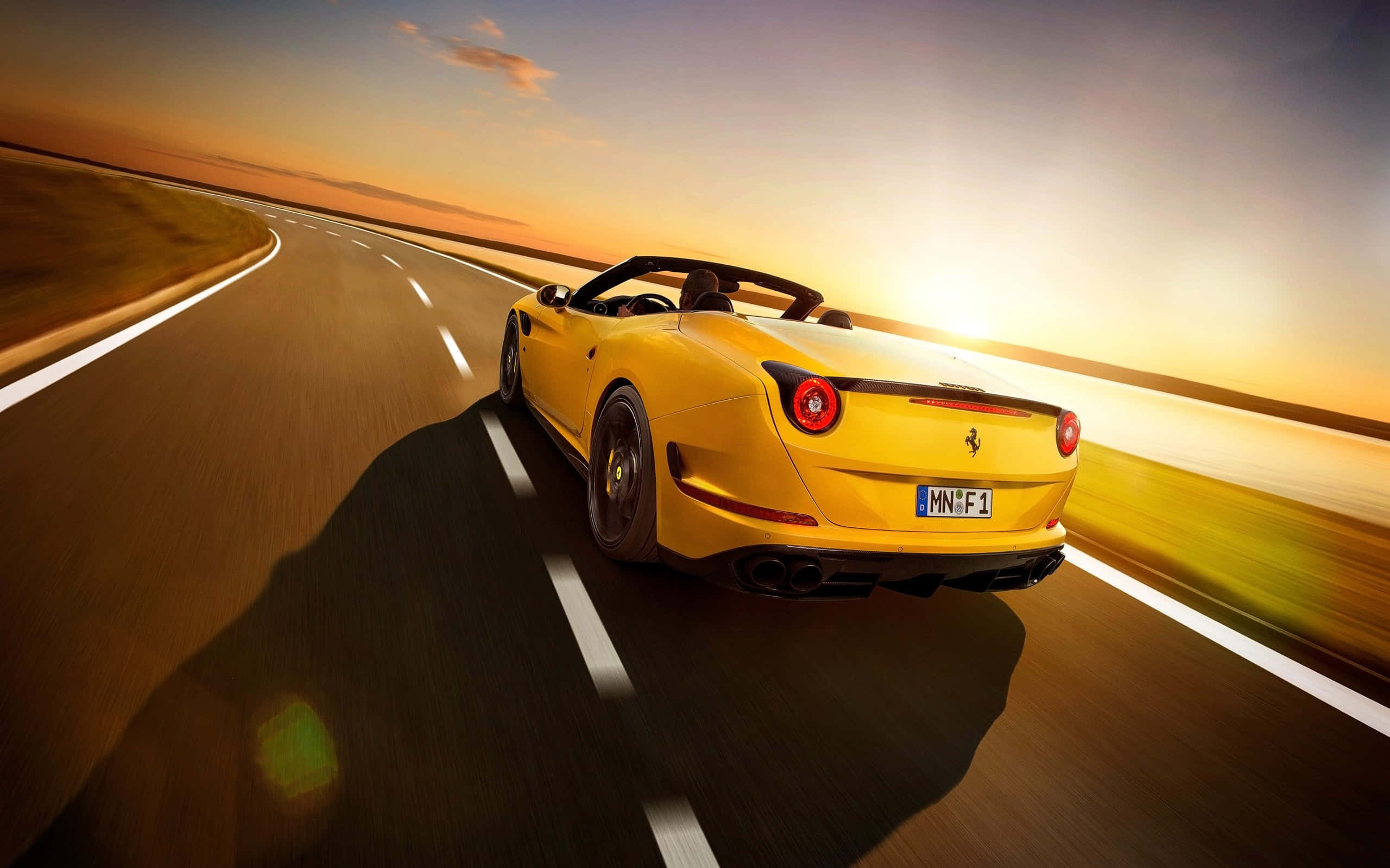 Ferrari California T 桌布 壁紙 — 一輛充滿活力的黃色法拉利敞篷車在日落時沿著蜿蜒的道路疾馳，投下長長的影子。