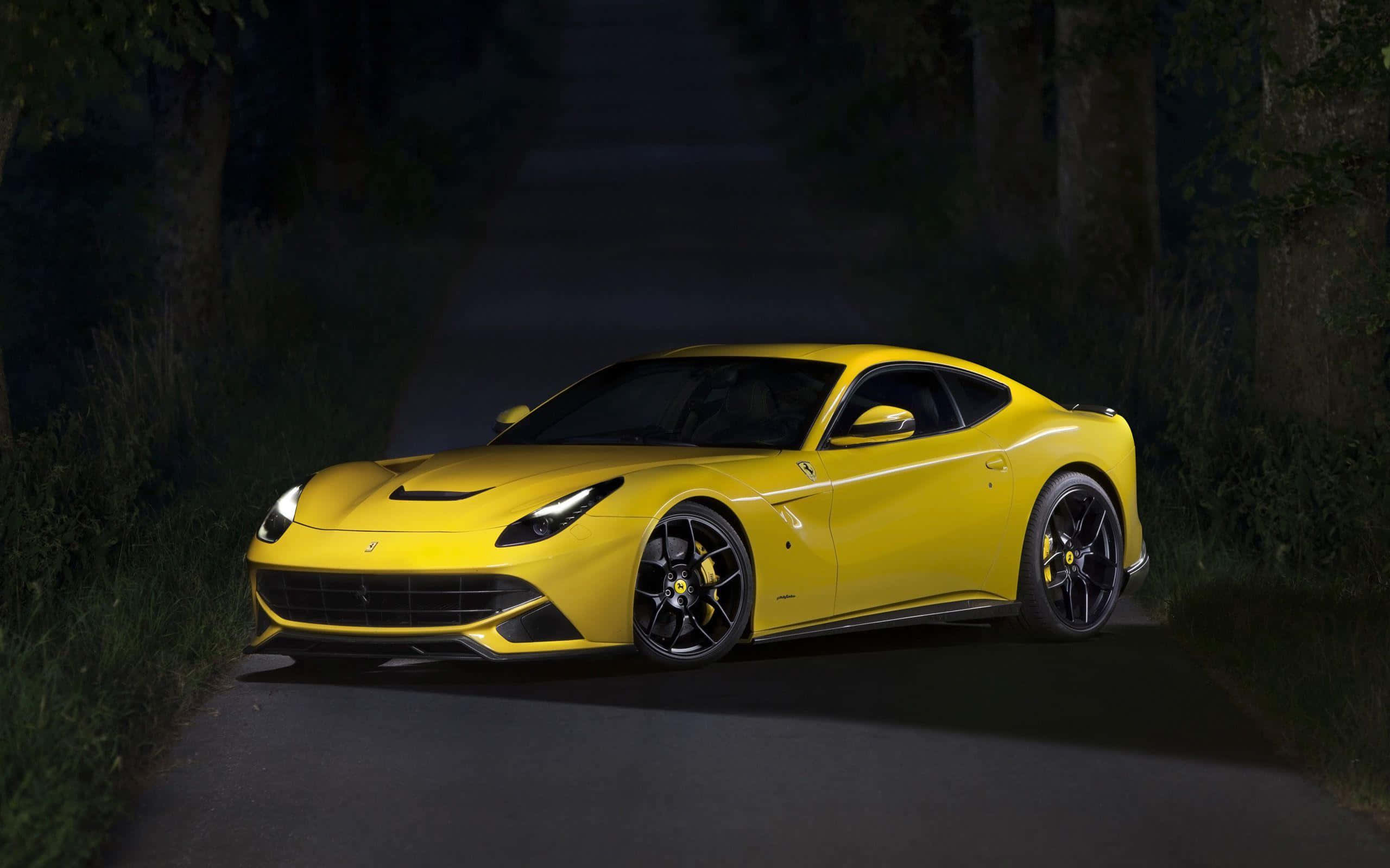 Ferrari F12 Berlinetta 桌布 壁紙 — 一輛充滿活力的黃色法拉利跑車在夜間黑暗的森林道路上，在車頭燈下閃耀。