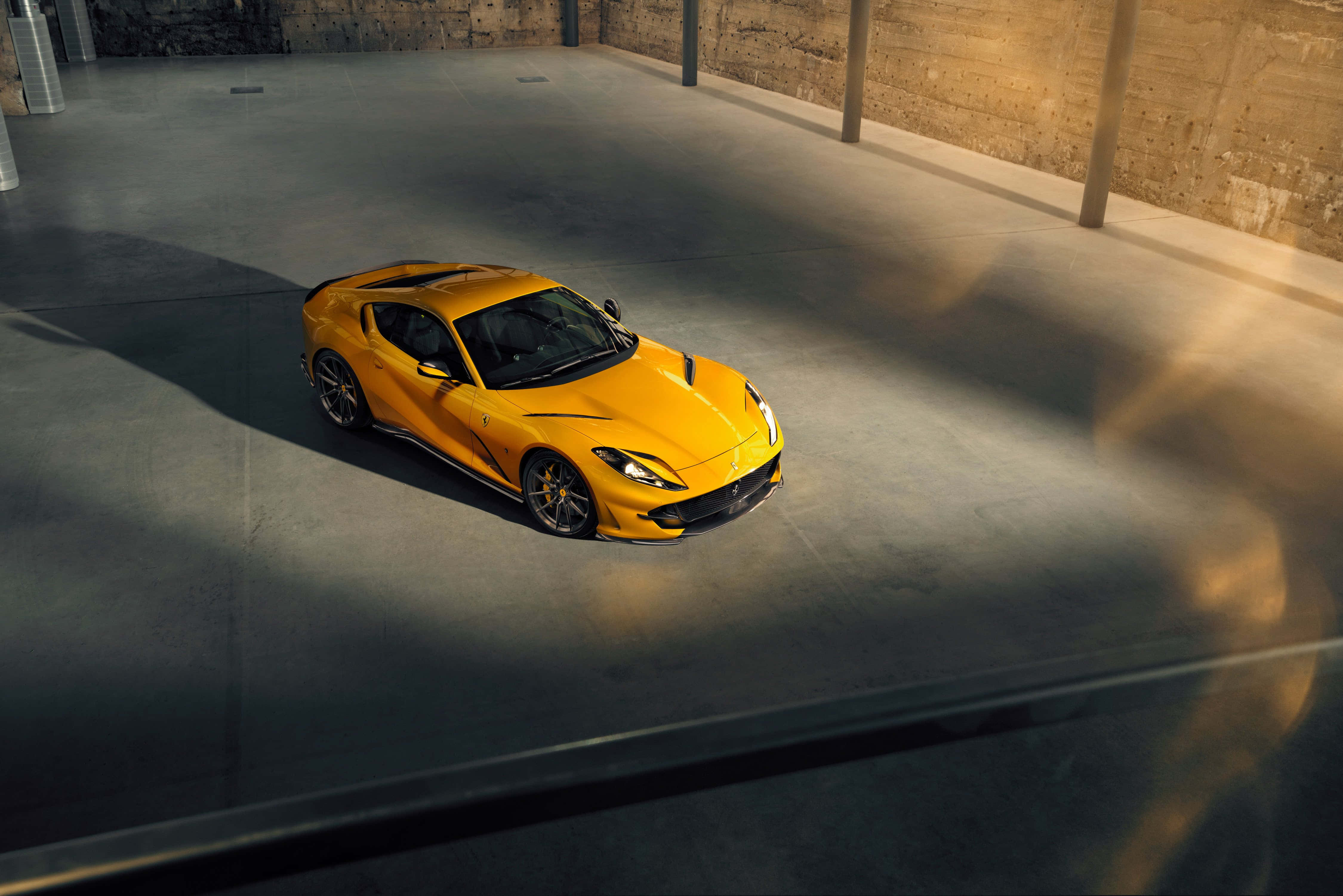 Ferrari 812 Superfast 桌布 壁紙 — 一輛充滿活力的黃色法拉利跑車在溫暖的陽光下閃耀，位於簡約的混凝土倉庫中。