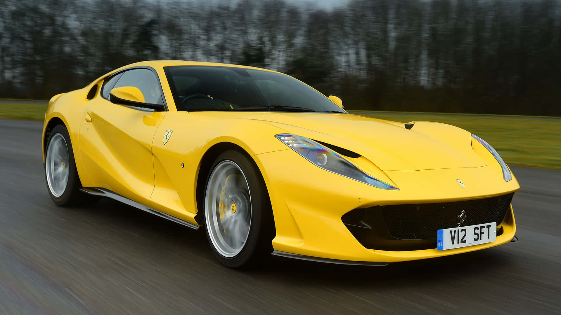 Ferrari 812 Superfast 桌布 壁紙 — 一輛充滿活力的黃色法拉利跑車在道路上疾馳，背景是模糊的樹木和草地。