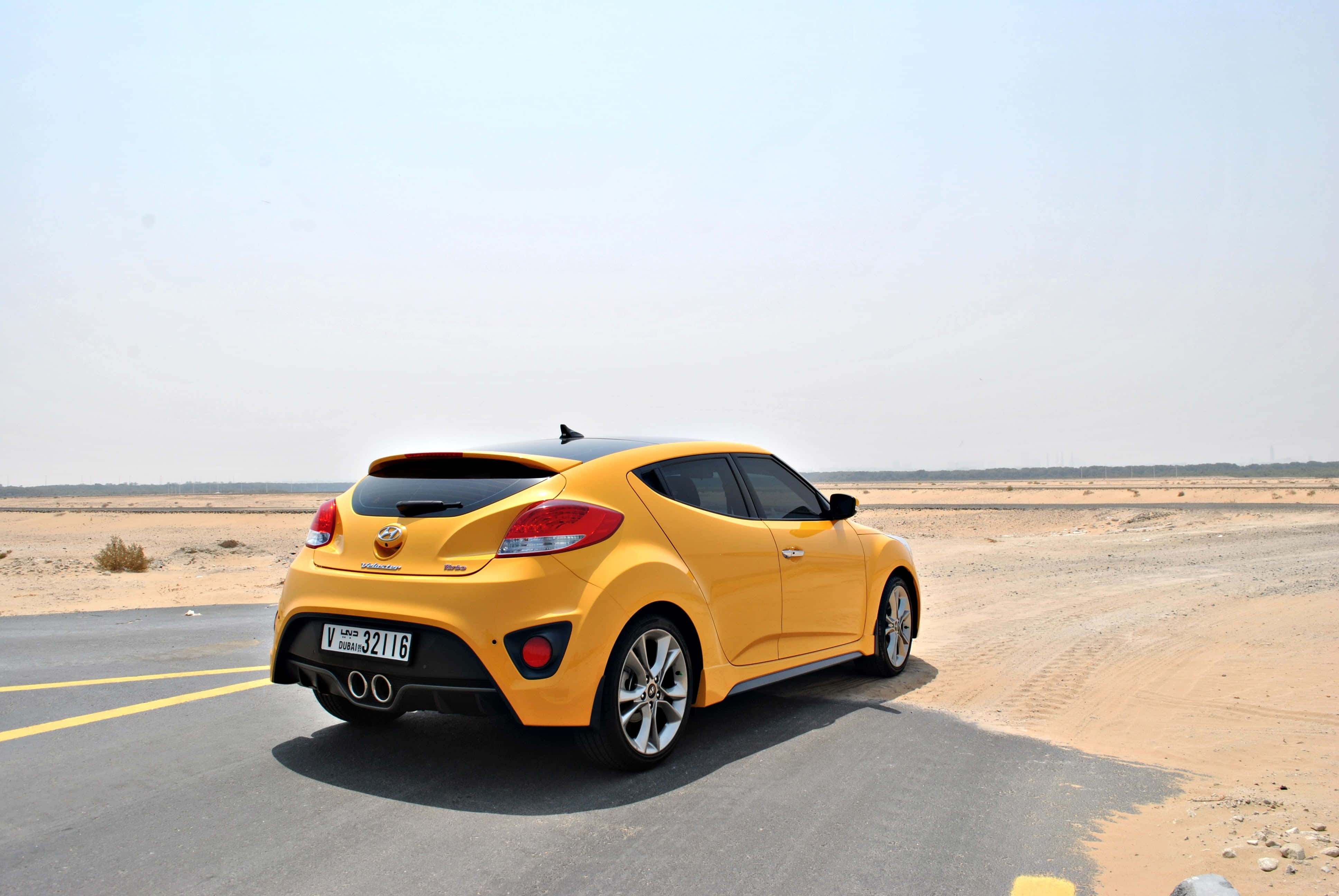 Hyundai Veloster 桌布 壁紙 — 一輛充滿活力的黃色現代Veloster跑車停泊在沙漠公路上，天空朦朧。