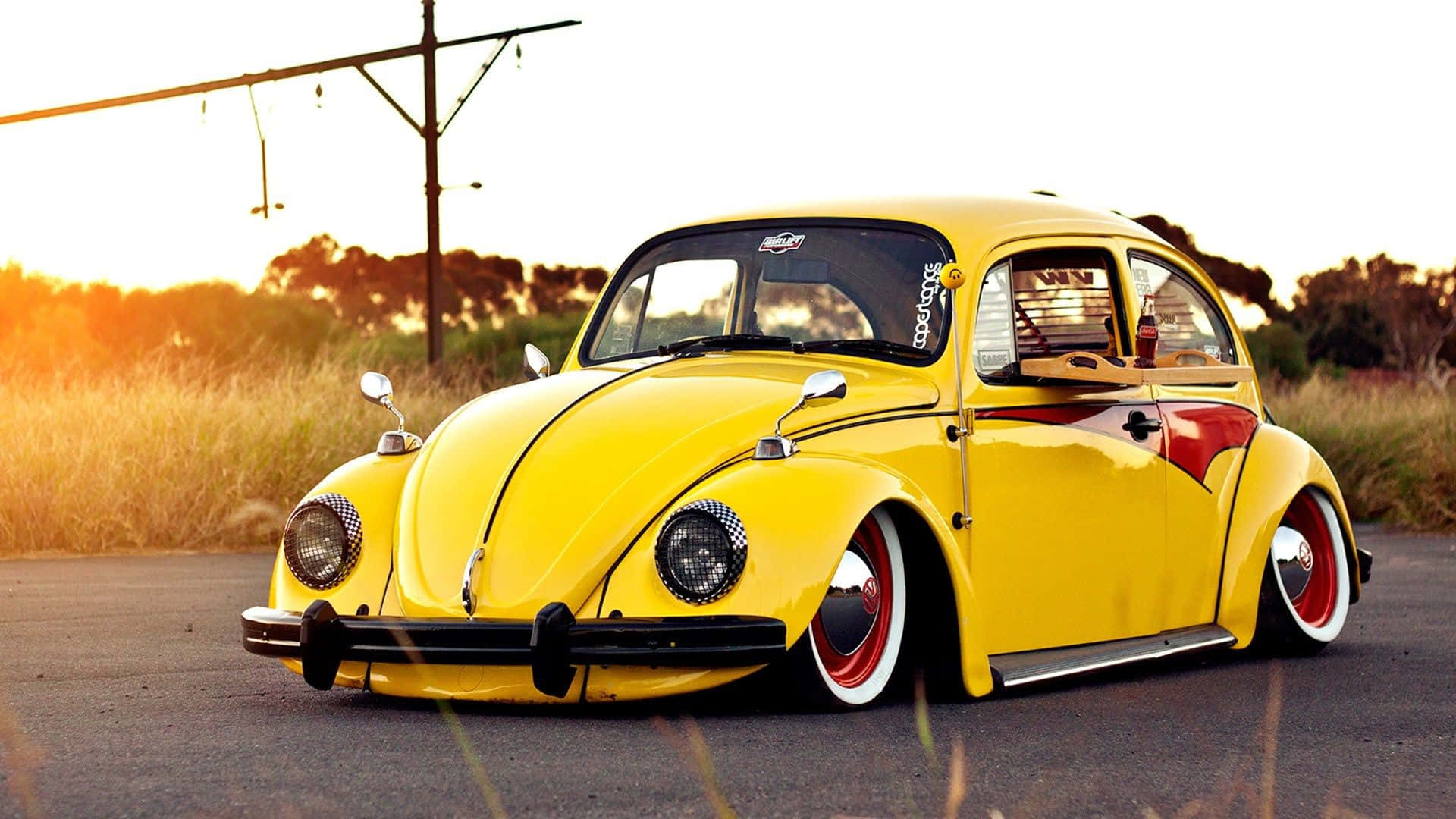 Yellow Car 桌布 壁紙 — 一輛充滿活力的黃色經典福士甲蟲車，帶有紅色點綴，低矮地停在金色日落時分的道路上。