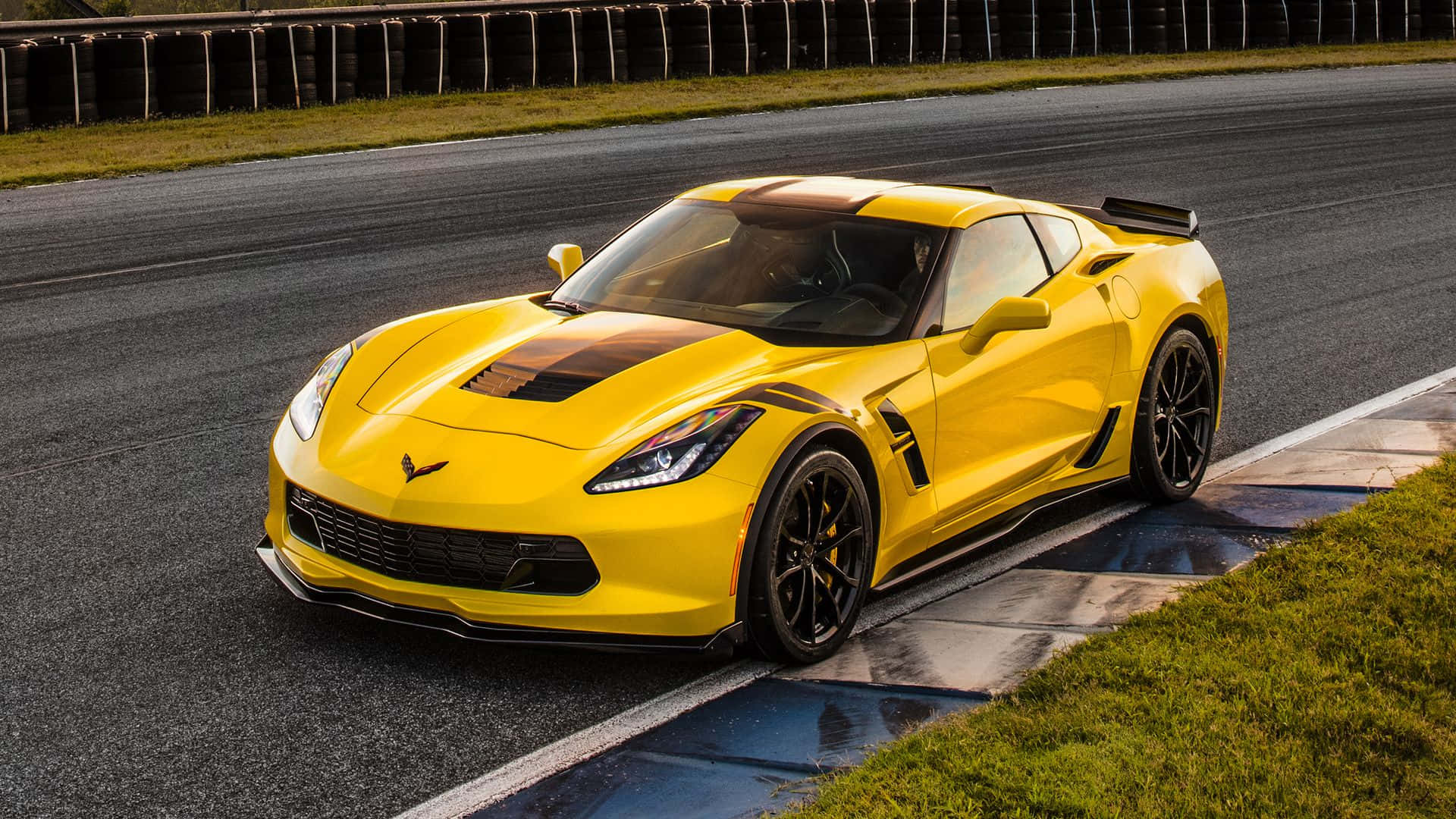 Chevrolet Corvette Grand Sport 桌布 壁紙 — 一輛充滿活力的黃色雪佛蘭Corvette跑車，帶有黑色點綴，停在潮濕的賽道上，旁邊是綠草。