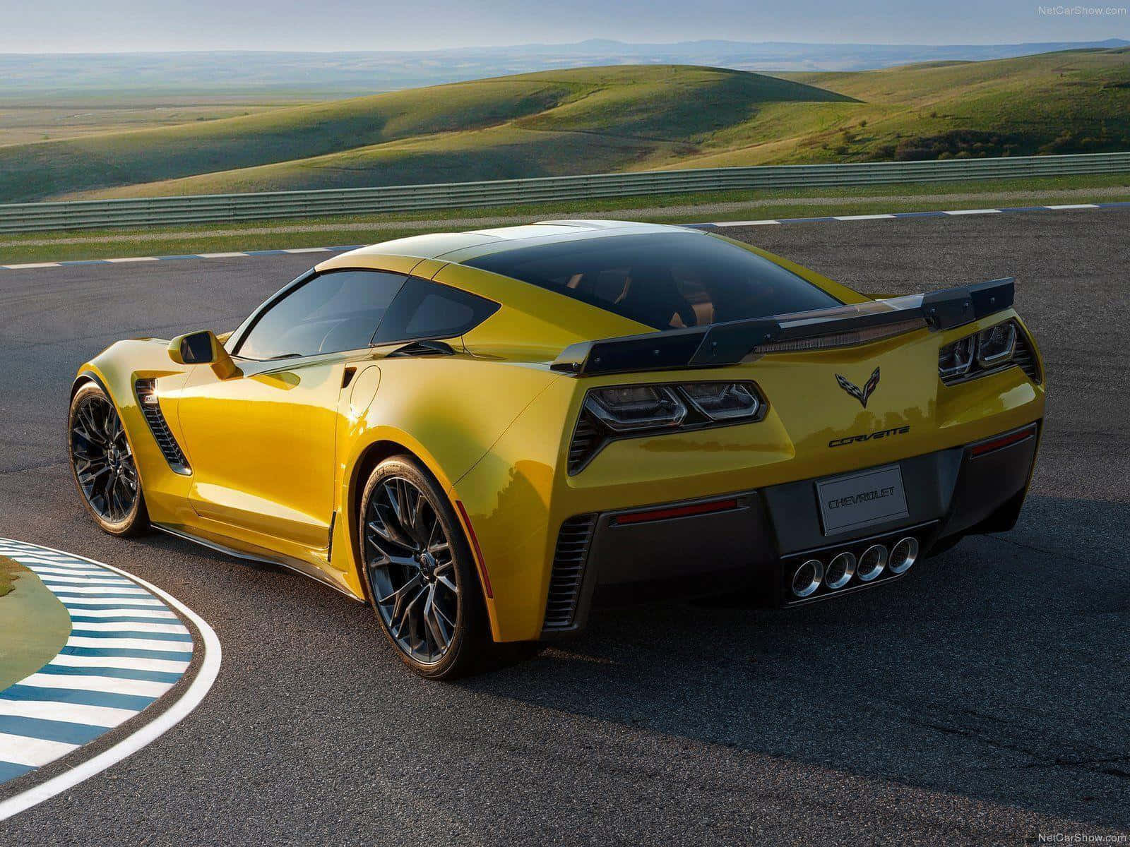 Chevrolet Corvette Z06 桌布 壁紙 — 一輛充滿活力的黃色雪佛蘭克爾維特跑車在蜿蜒的賽道上疾馳，背景是連綿起伏的綠色山丘。