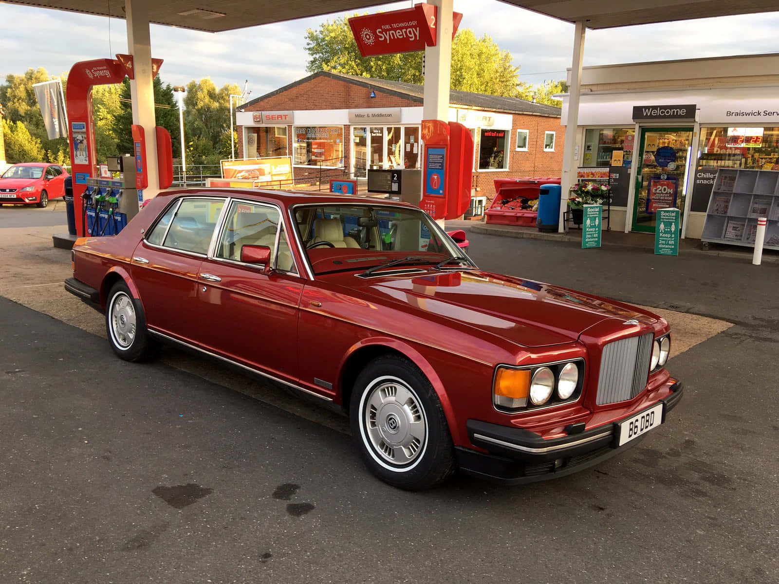 Bentley Eight 桌布 壁紙 — 一輛光亮的紅色 Bentley Turbo R 停泊在加油站，背景有便利店和樹木。