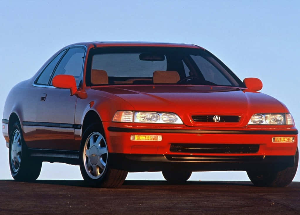 Acura Legend 桌布 壁紙 — 一輛光亮的紅色Acura轎跑車在明亮的日光下，在深色路面上映襯著清澈的藍天閃閃發光。