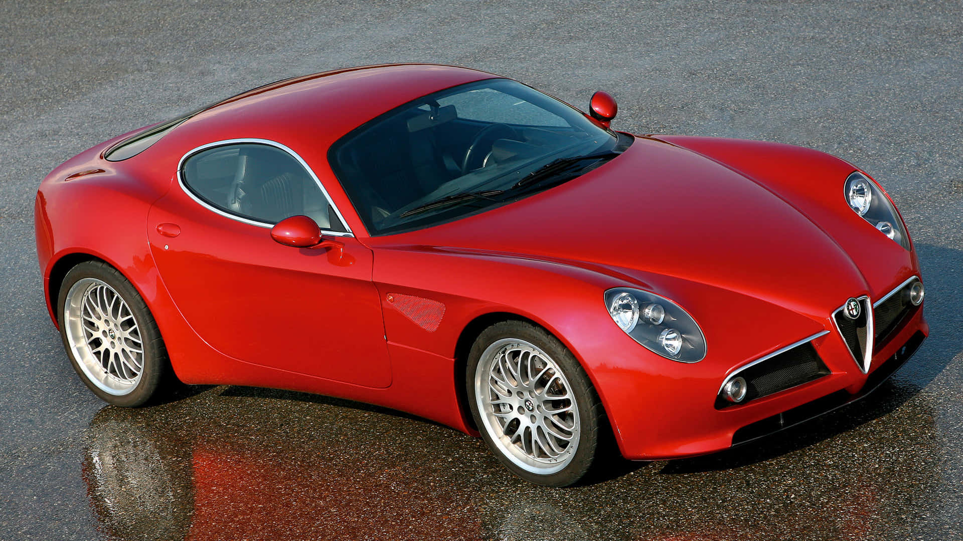 Alfa Romeo 8c Competizione 桌布 壁紙 — 一輛光亮的紅色Alfa Romeo跑車在潮濕的瀝青路上，於明亮的日光下閃耀，倒影清晰可見。
