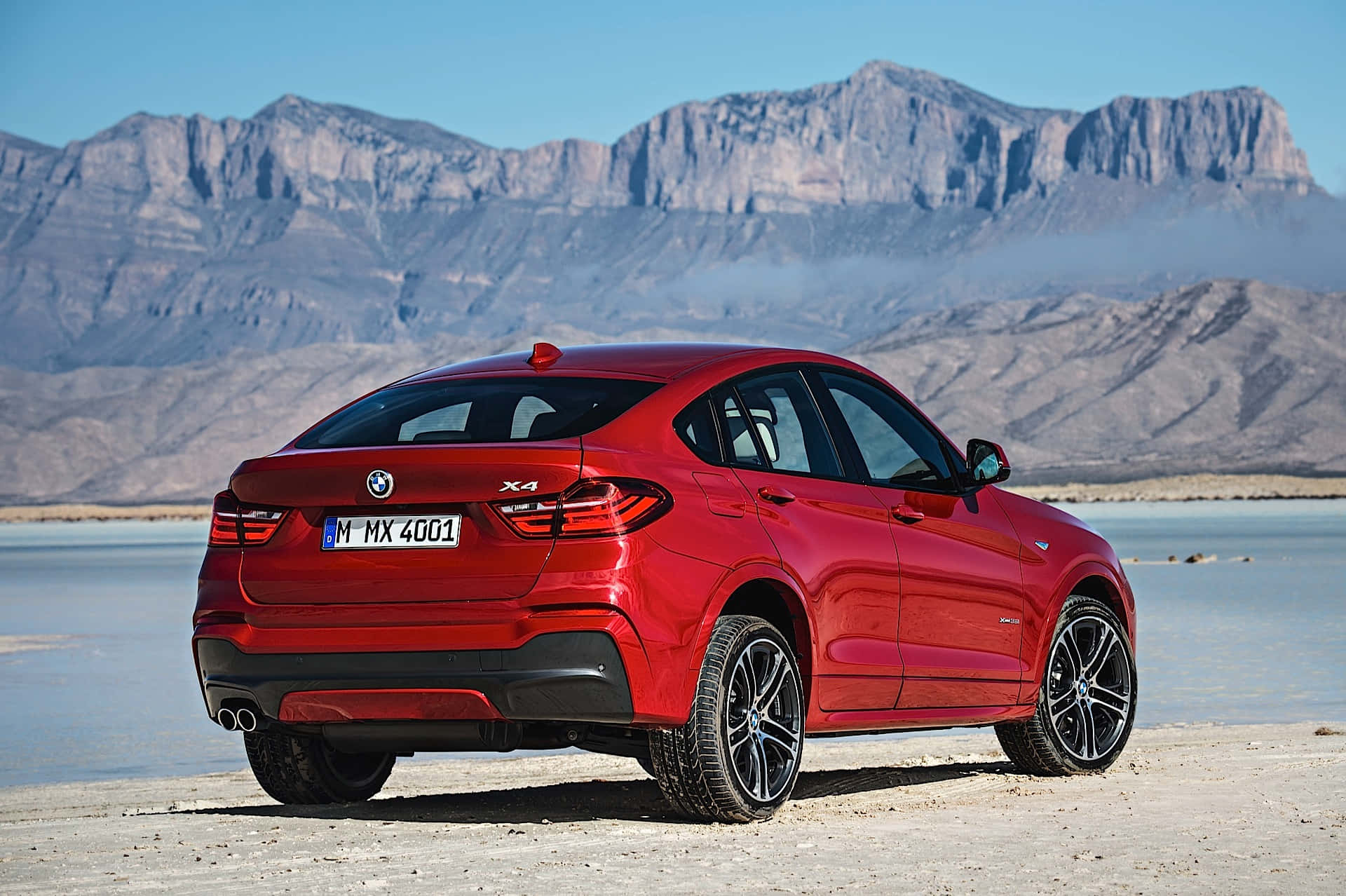 Bmw X4 桌布 壁紙 — 一輛光亮的紅色BMW X4 SUV停在乾涸的湖床上，背後是崎嶇的山脈，上方是清澈的藍天。
