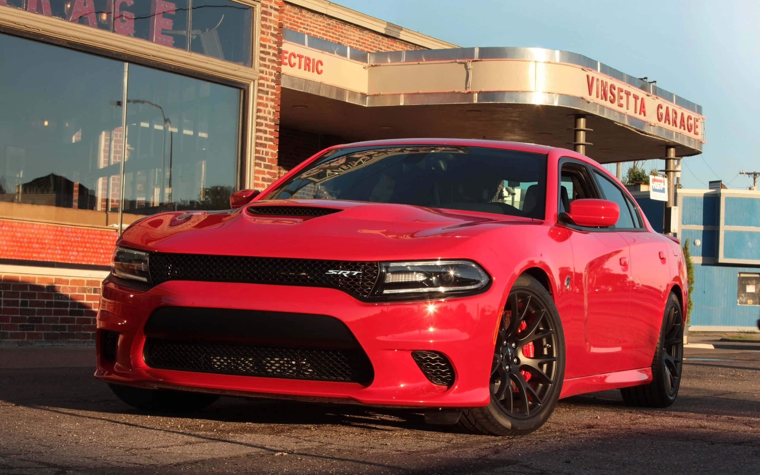 Dodge Charger 桌布 壁紙 — 一輛光亮的紅色Dodge Charger SRT停在一間復古磚砌車庫前，背景是晴朗的藍天。