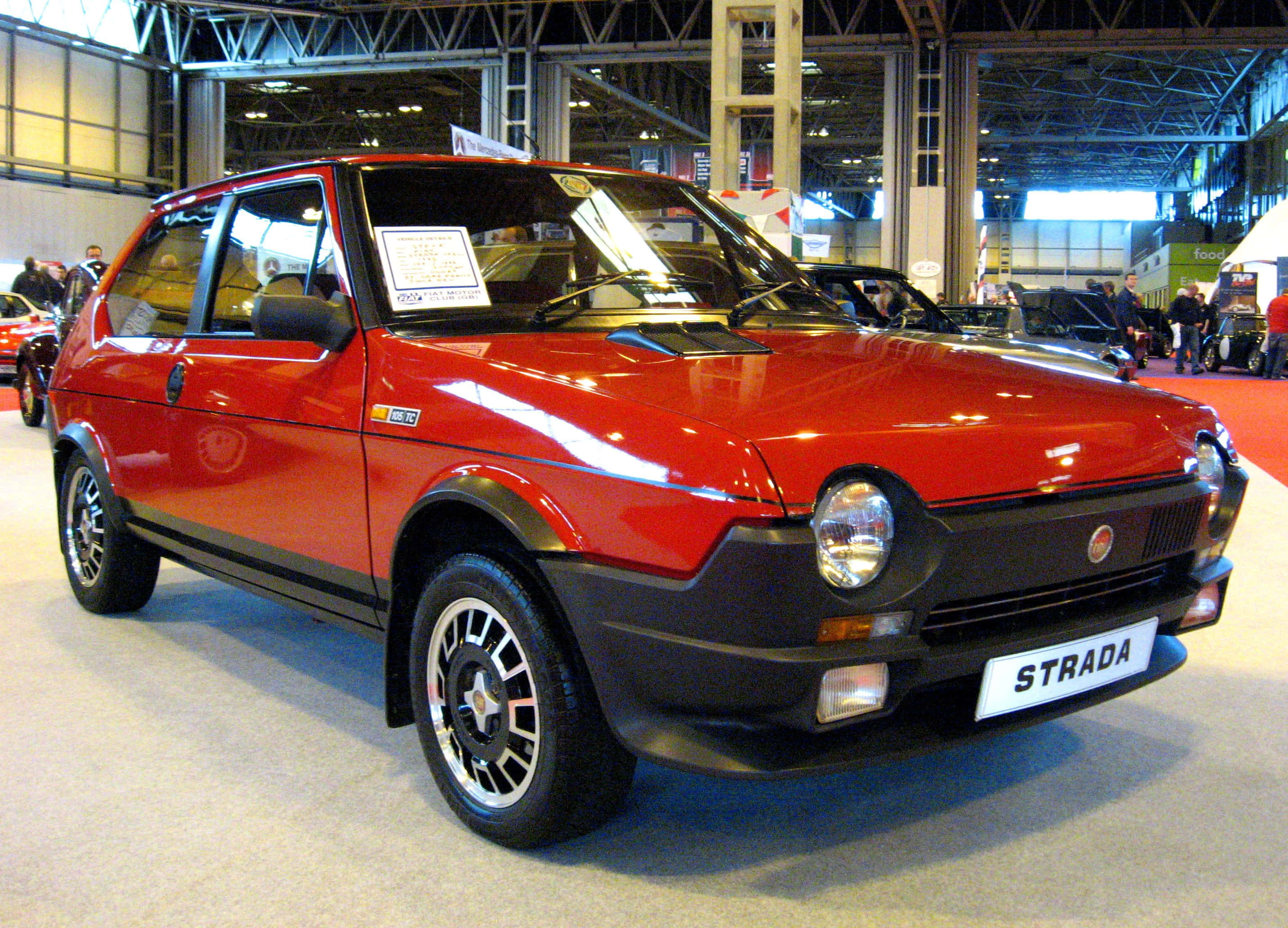Fiat Ritmo 桌布 壁紙 — 一輛光亮的紅色Fiat Strada掀背車在室內車展中展出，地板拋光，頭頂有燈光。