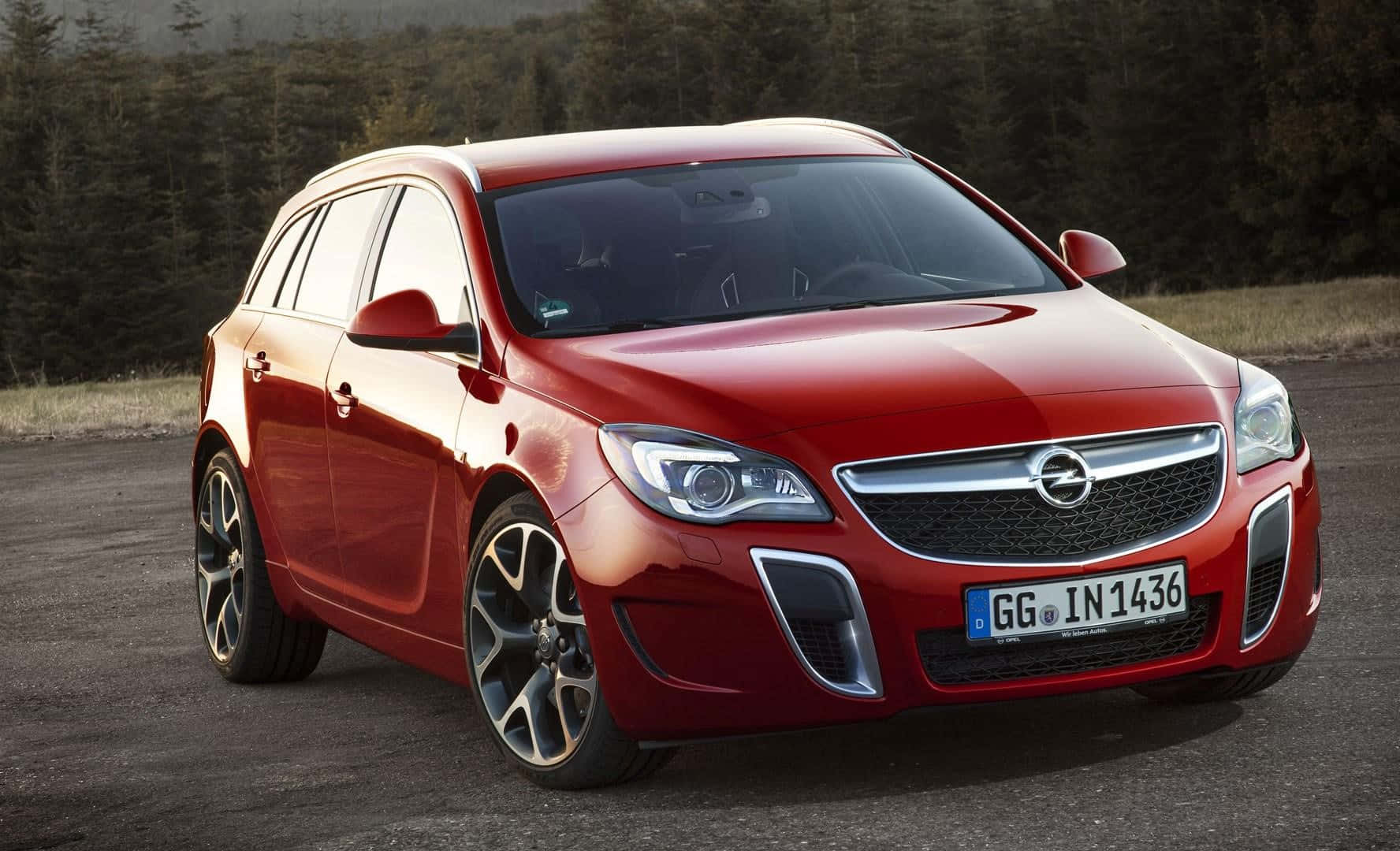 Opel Insignia 桌布 壁紙 — 一輛光亮的紅色Opel Insignia Sports Tourer停在碎石上，背景是森林，在柔和日光下。