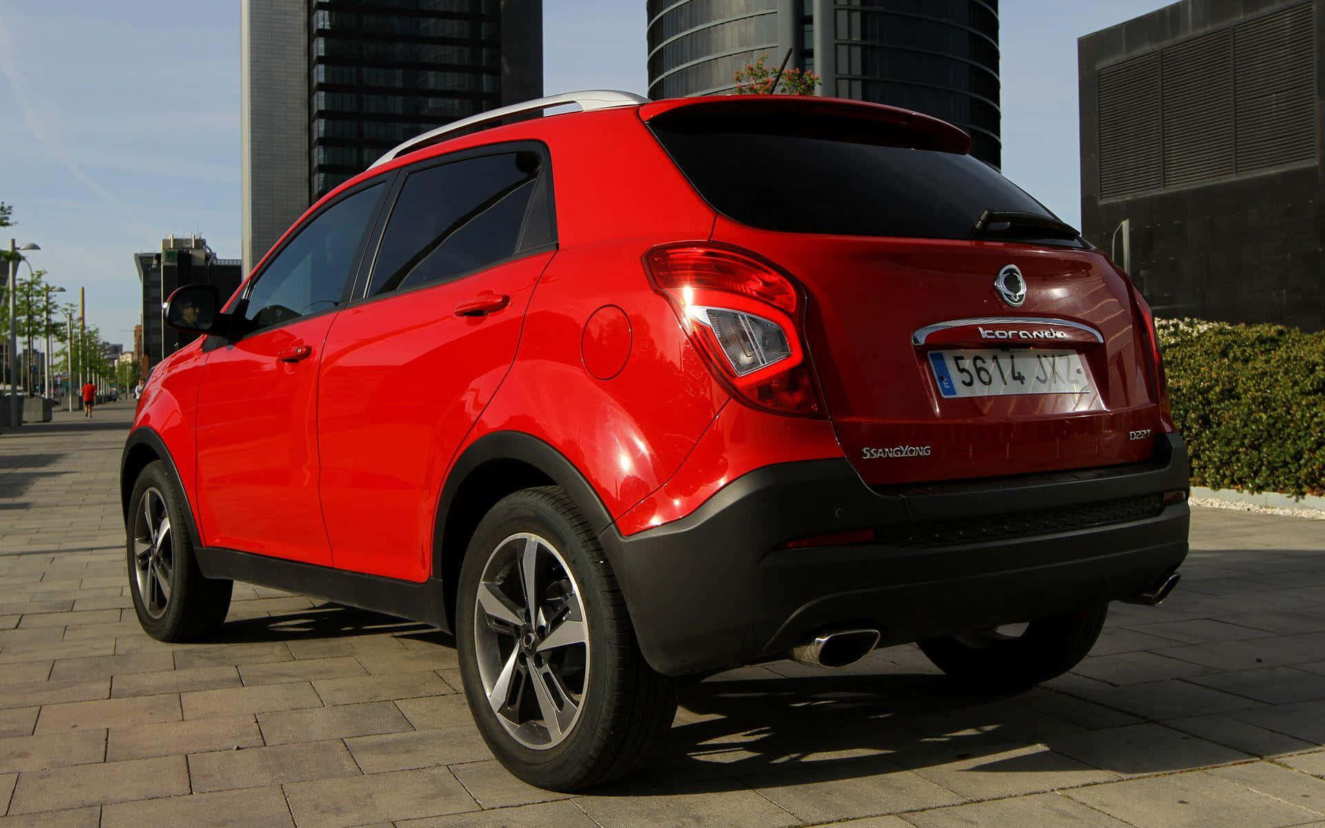 Ssangyong 桌布 壁紙 — 一輛光亮的紅色SsangYong Korando SUV停泊在鋪砌的都市廣場上，背景是現代建築。