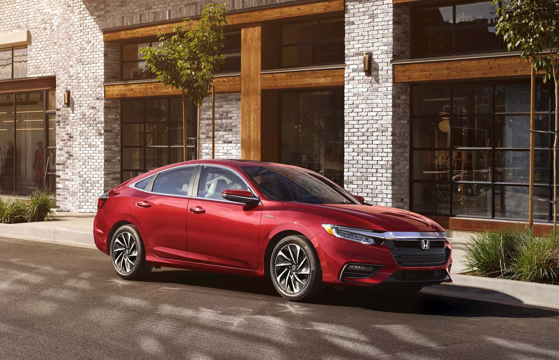 Honda Insight 桌布 壁紙 — 一輛光亮的紅色本田房車停泊在陽光普照的街道上，旁邊是一座現代磚木建築。