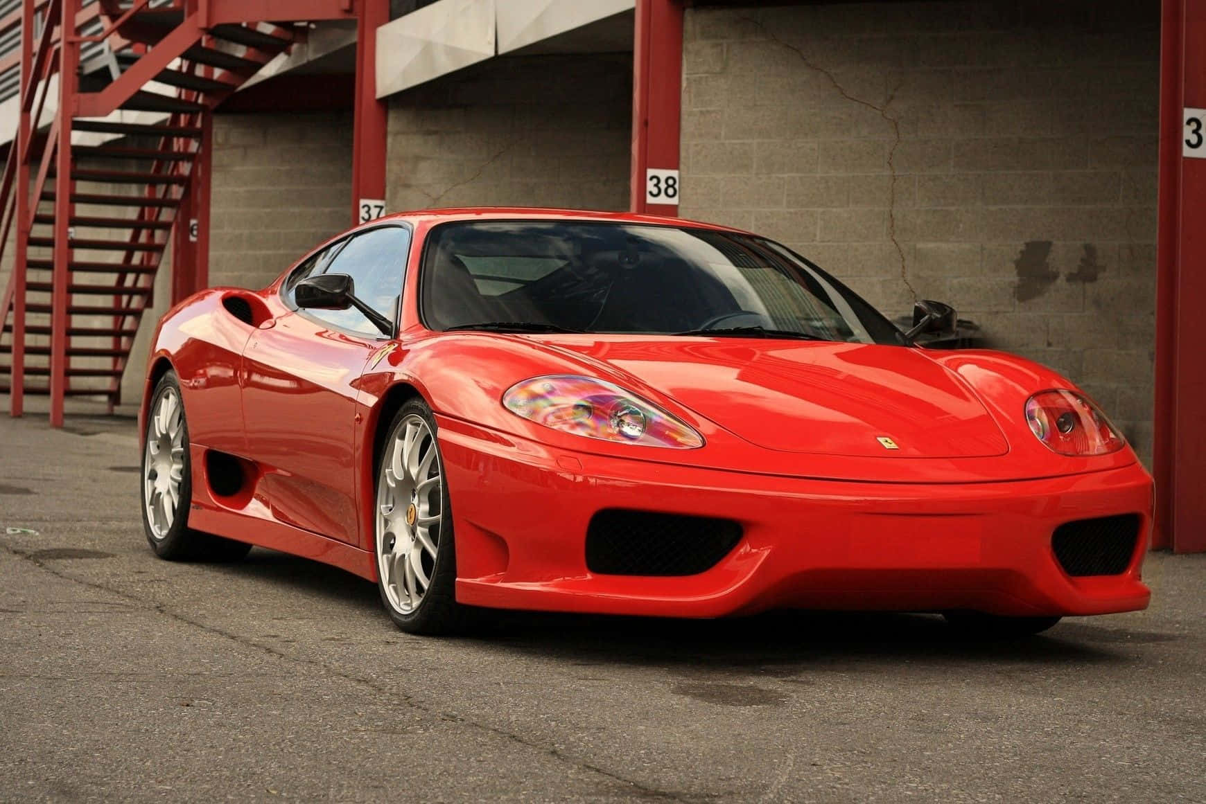 Ferrari 360 Modena 桌布 壁紙 — 一輛光亮的紅色法拉利360跑車停放在一個設有紅色金屬樓梯和編號車位的混凝土車庫中。