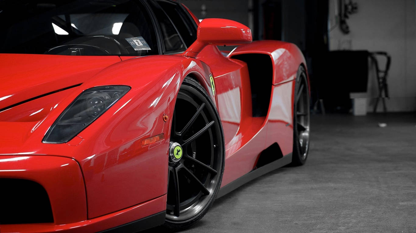 Sports Car 桌布 壁紙 — 一輛光亮的紅色法拉利Enzo停放在光線昏暗的車庫中，配備黑色車輪和流線型空氣動力學線條。