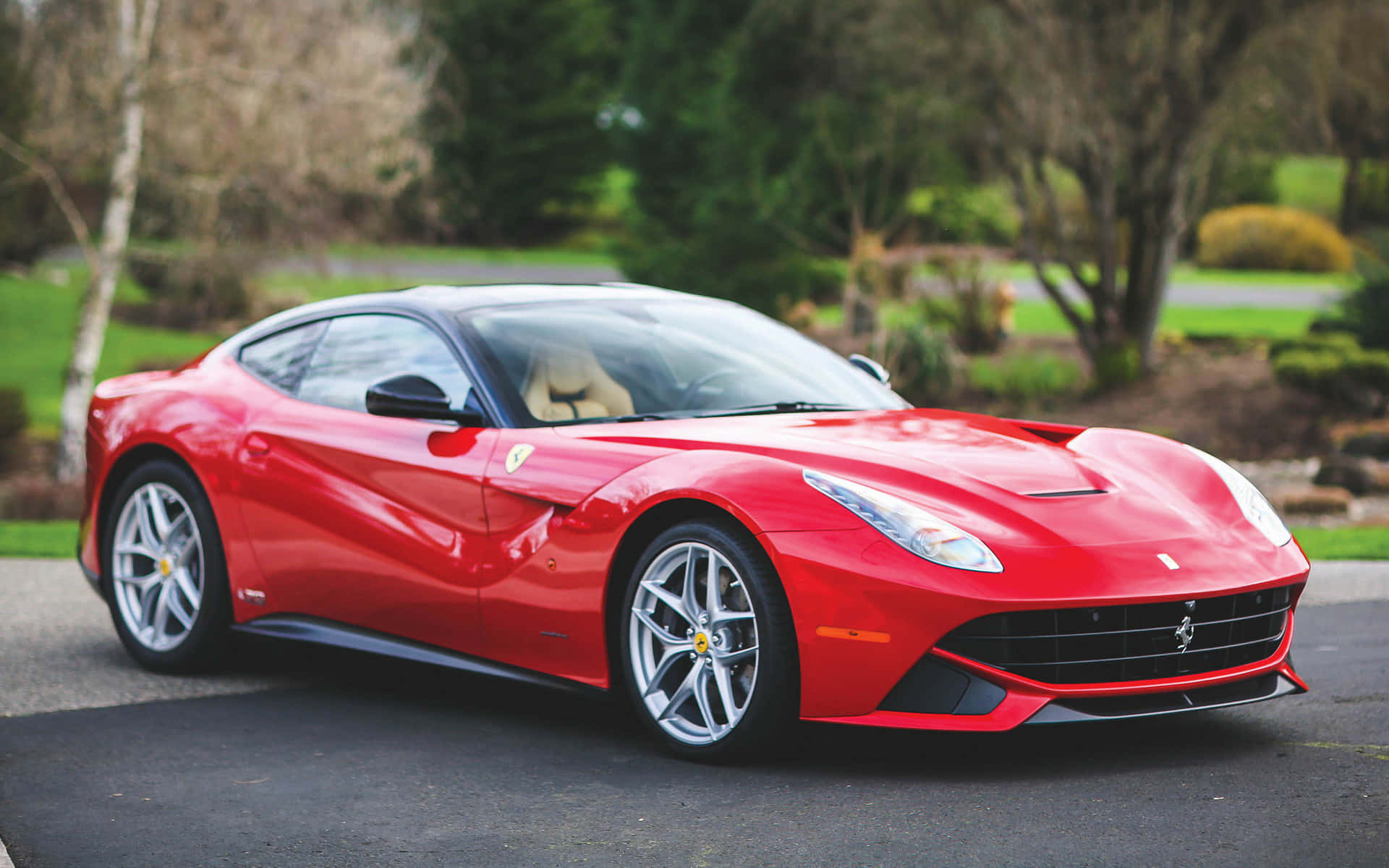 Ferrari F12 Berlinetta 桌布 壁紙 — 一輛光亮的紅色法拉利F12tdf跑車停在瀝青路上，背景有綠樹和灌木。