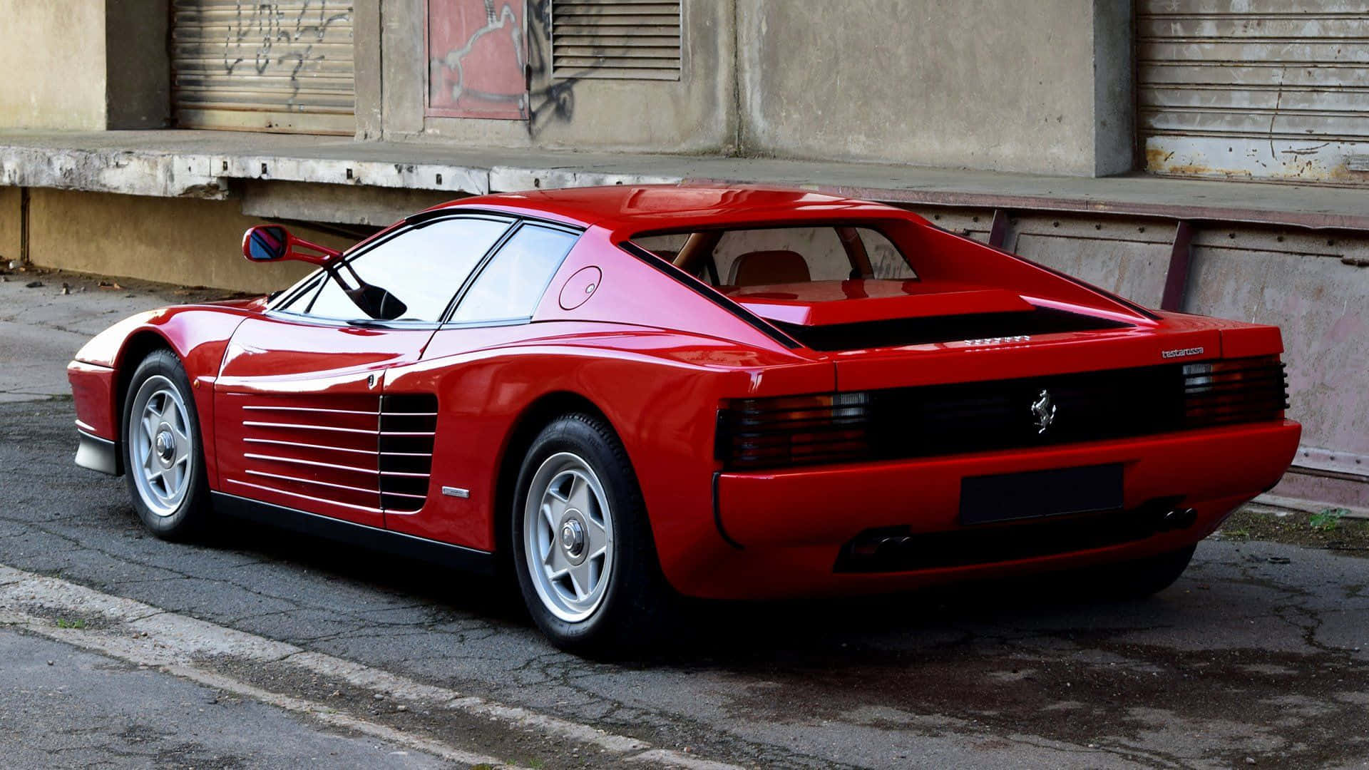 Ferrari Testarossa 桌布 壁紙 — 一輛光亮的紅色法拉利Testarossa停泊在佈滿裂痕的城市街道上，旁邊是帶有塗鴉的風化混凝土牆。
