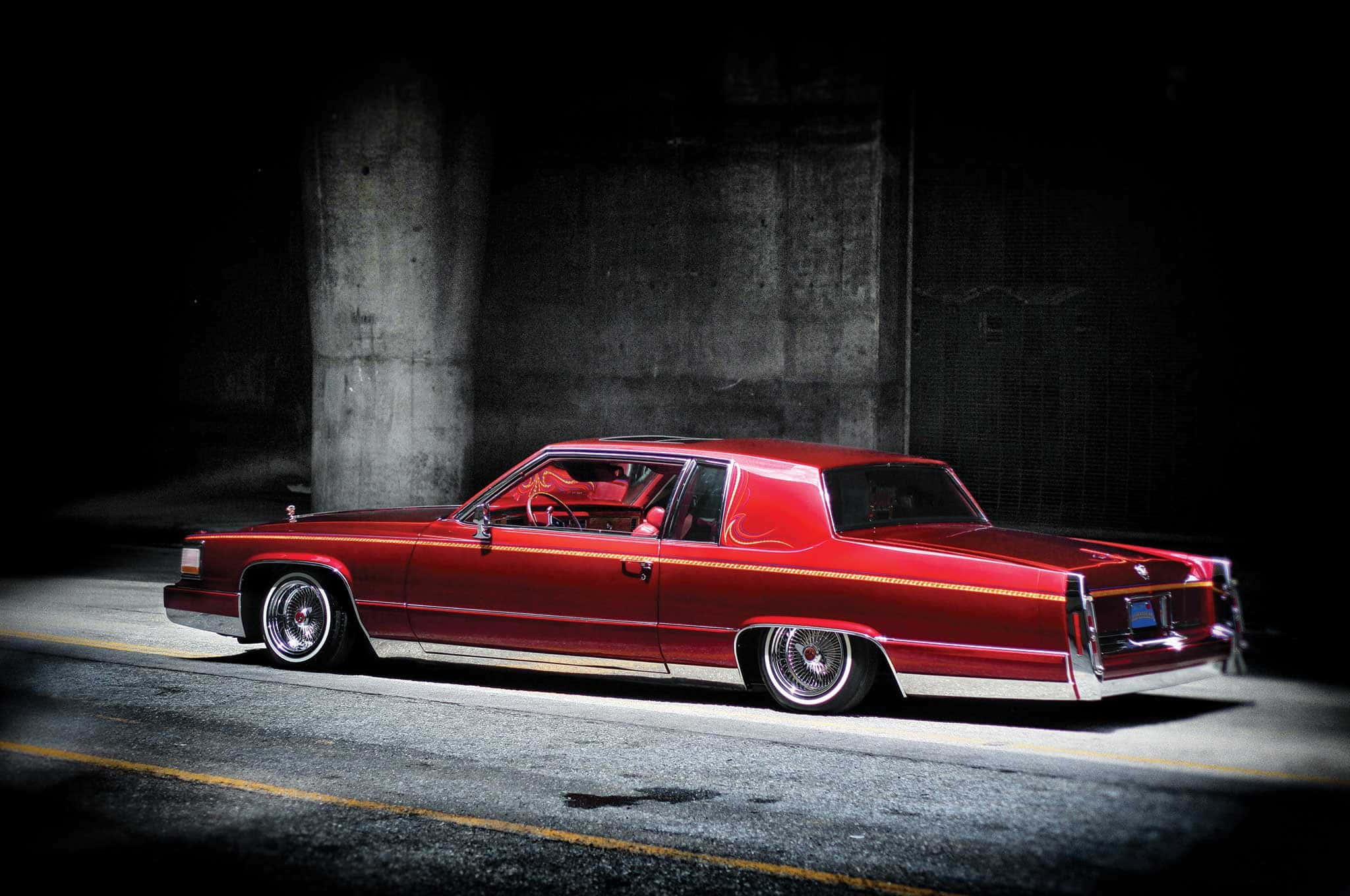Cadillac Deville 桌布 壁紙 — 一輛光亮的紅色經典汽車配備定制輪圈，在夜晚的混凝土天橋下被戲劇性地照亮。
