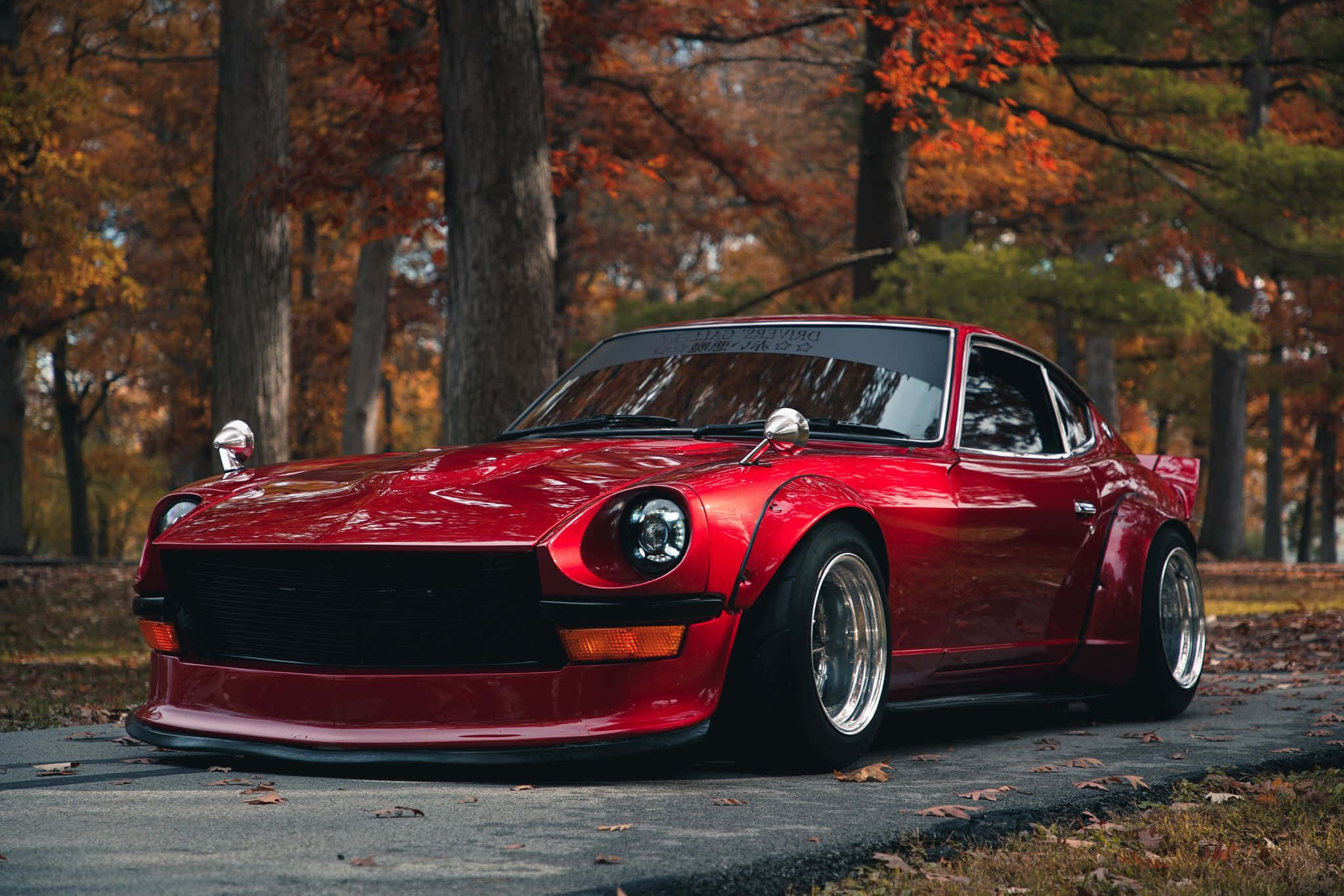 Datsun 桌布 壁紙 — 一輛光亮的紅色經典跑車停泊在落葉滿佈的森林道路上，秋樹環繞。