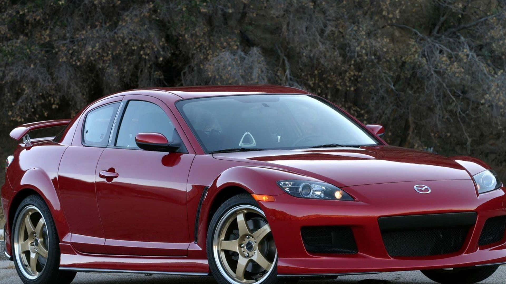 Mazda Rx-8 桌布 壁紙 — 一輛光亮的紅色萬事得RX-8跑車配金色輪圈，停泊在瀝青路上，背景是乾枯的樹木。