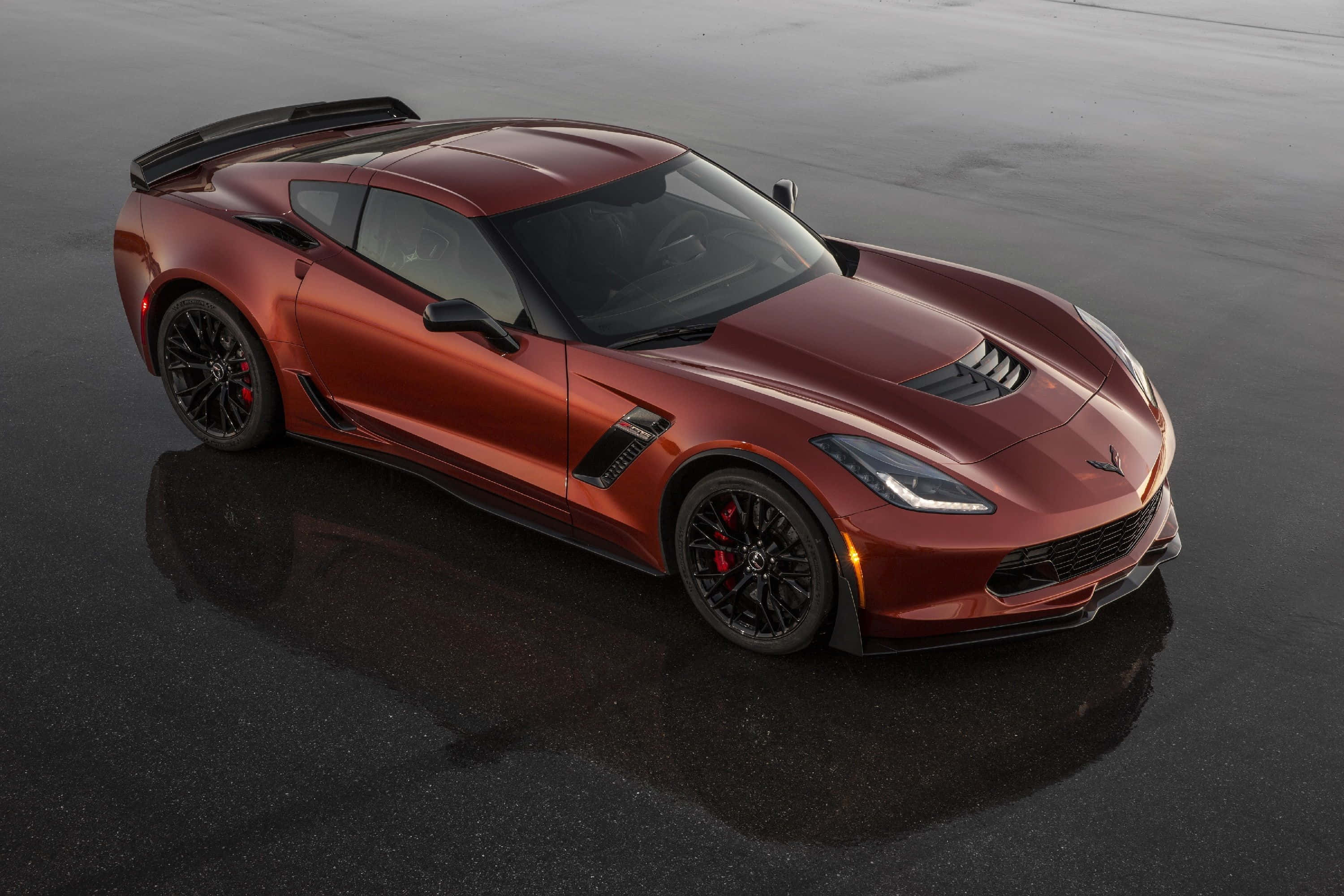 Chevrolet Corvette Z06 桌布 壁紙 — 一輛光亮的紅色跑車，帶有黑色飾件和紅色制動卡鉗，停在潮濕的瀝青路面上，反射出其流線型設計。