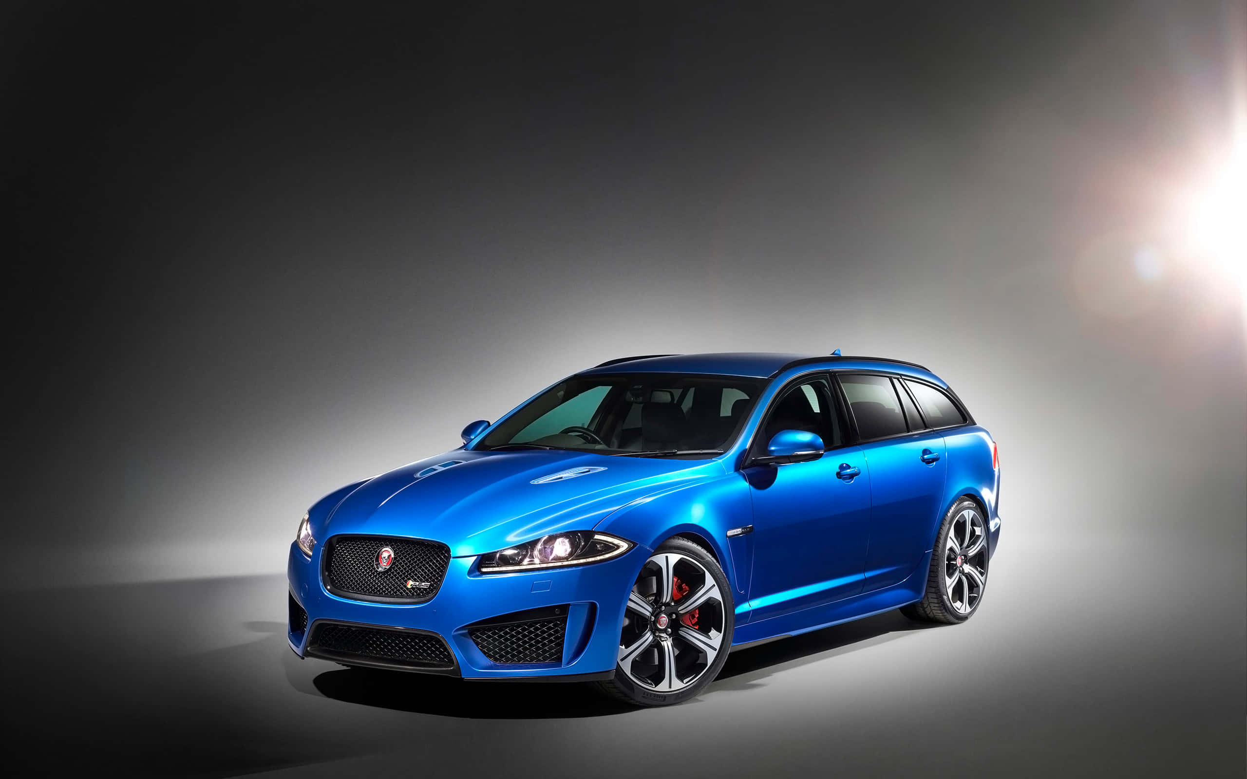 Jaguar Xfr 桌布 壁紙 — 一輛光亮的藍色Jaguar XF Sportbrake在暗色漸變背景下的戲劇性工作室燈光中閃耀。