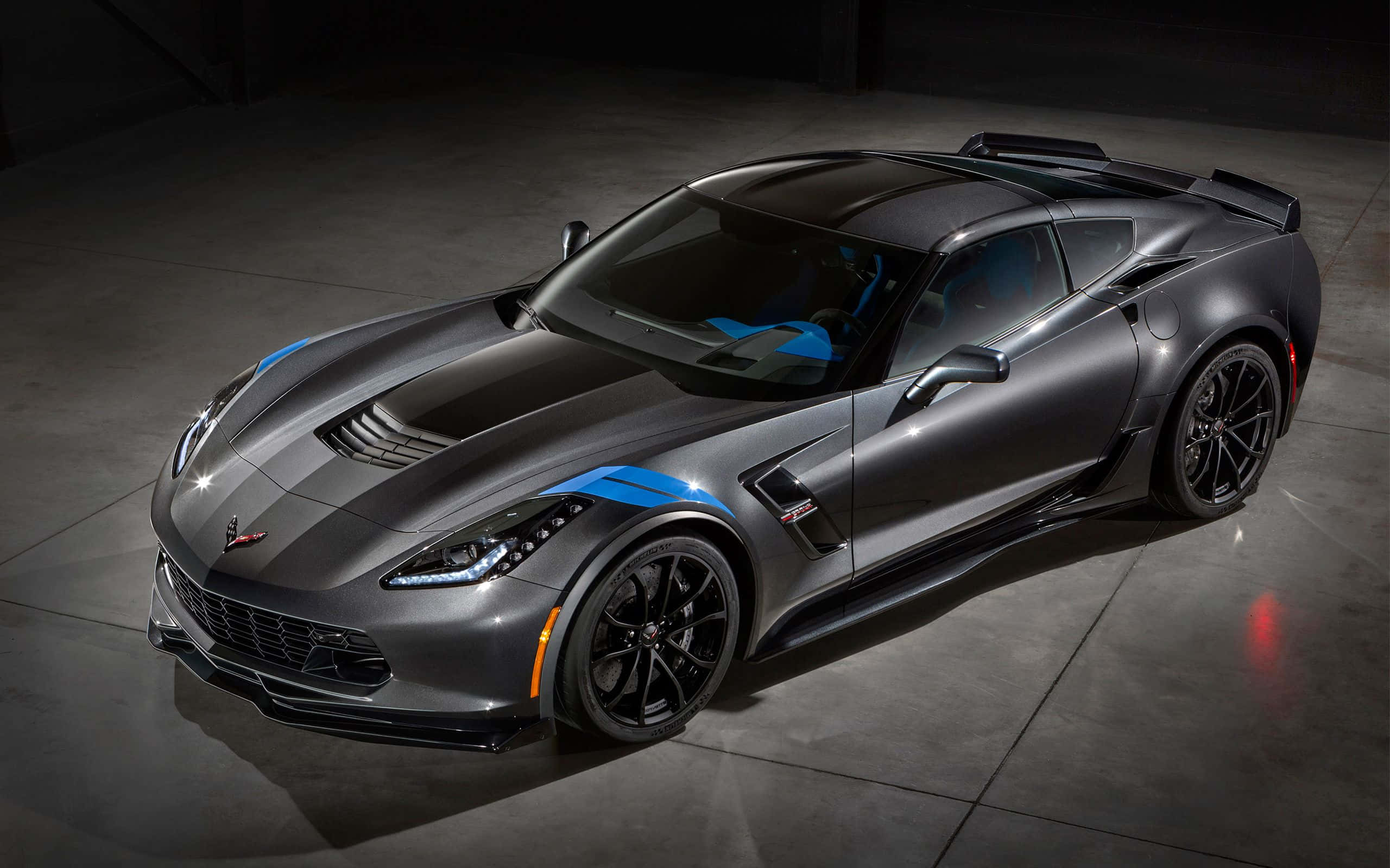 corvette 桌布 壁紙 — 一輛光滑的啞光灰色Corvette跑車，帶有醒目的藍色賽車條紋，在黑暗的混凝土車庫中，在攝影棚燈光下閃閃發光。