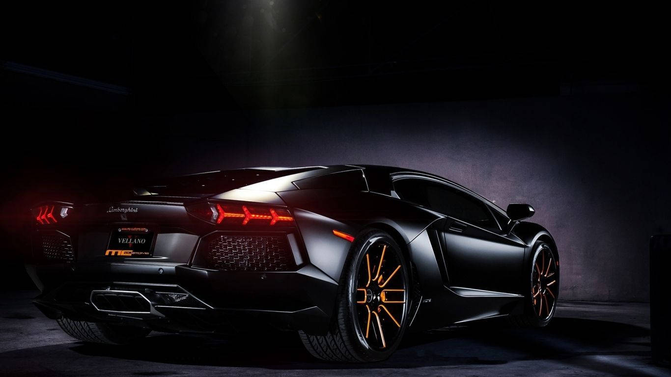Sports Car 桌布 壁紙 — 一輛光滑的啞光黑色林寶堅尼Aventador，帶有發光的橙色飾邊和紅色尾燈，在黑暗的車庫中戲劇性地照亮。