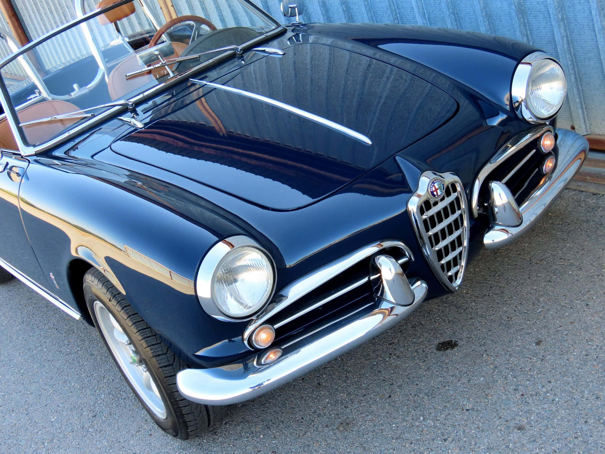 Alfa Romeo Spider 桌布 壁紙 — 一輛光澤深藍色經典愛快羅密歐Spider開篷車在明亮日光下閃耀，帶有鍍鉻飾邊和可見的米色內飾。