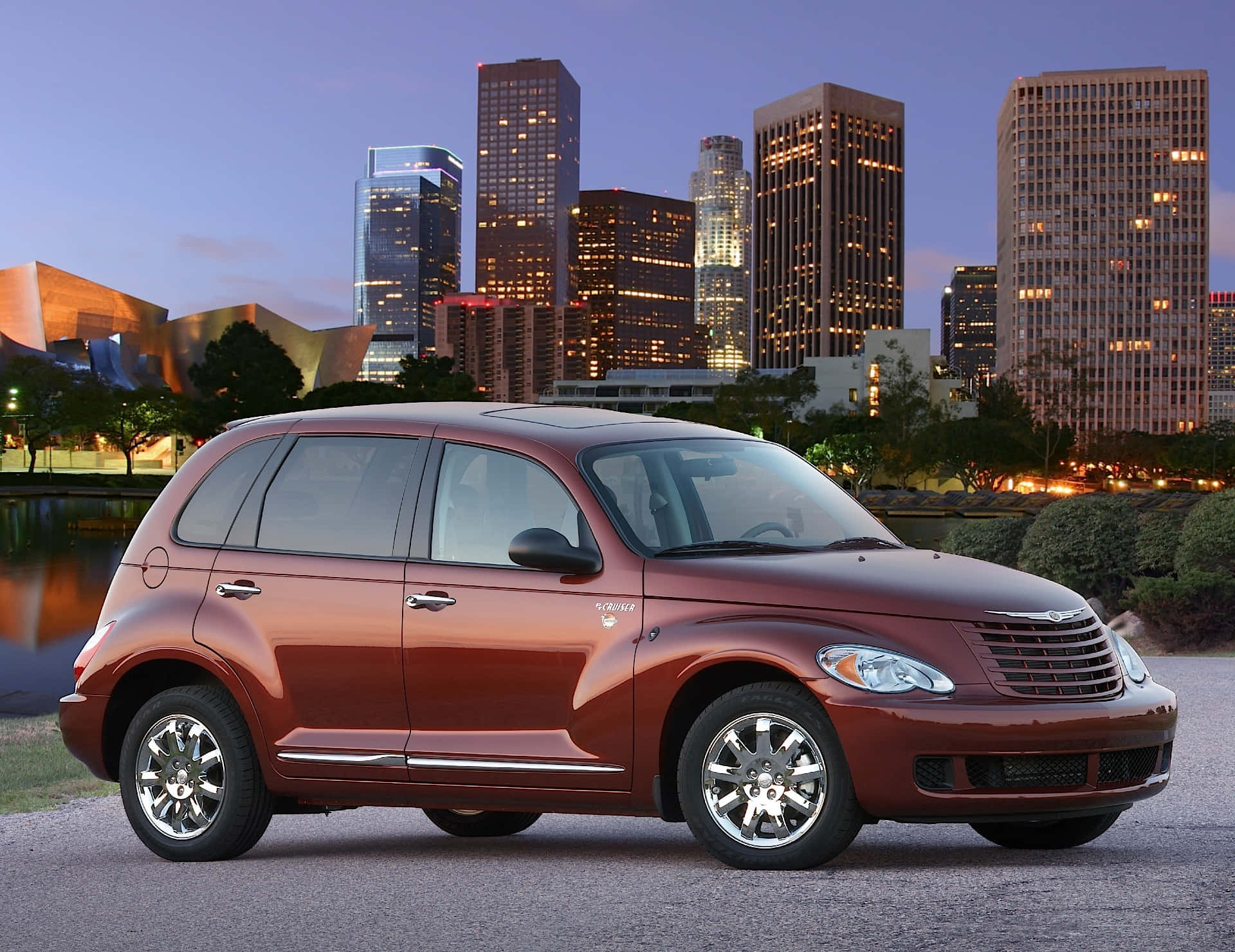 Chrysler Pt Cruiser 桌布 壁紙 — 一輛光澤的栗色PT Cruiser停在行人路上，背後是暮色中的城市天際線和亮燈的摩天大樓。