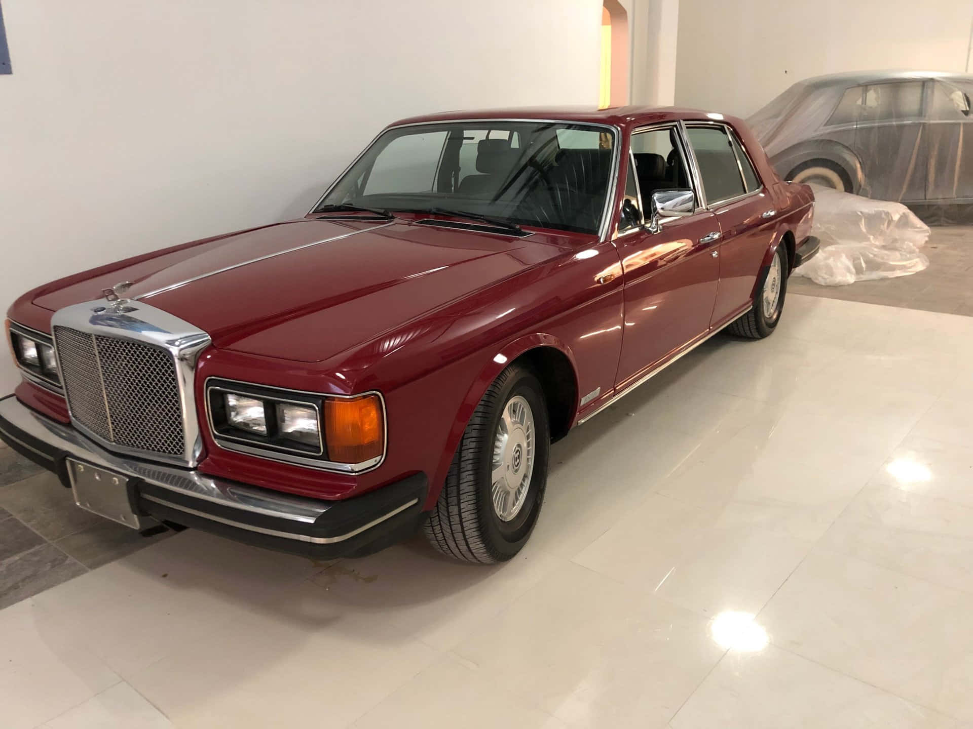 Bentley Eight 桌布 壁紙 — 一輛光澤的栗色賓利T系列轎車在明亮的燈光下，在純白色瓷磚陳列室中閃閃發光。