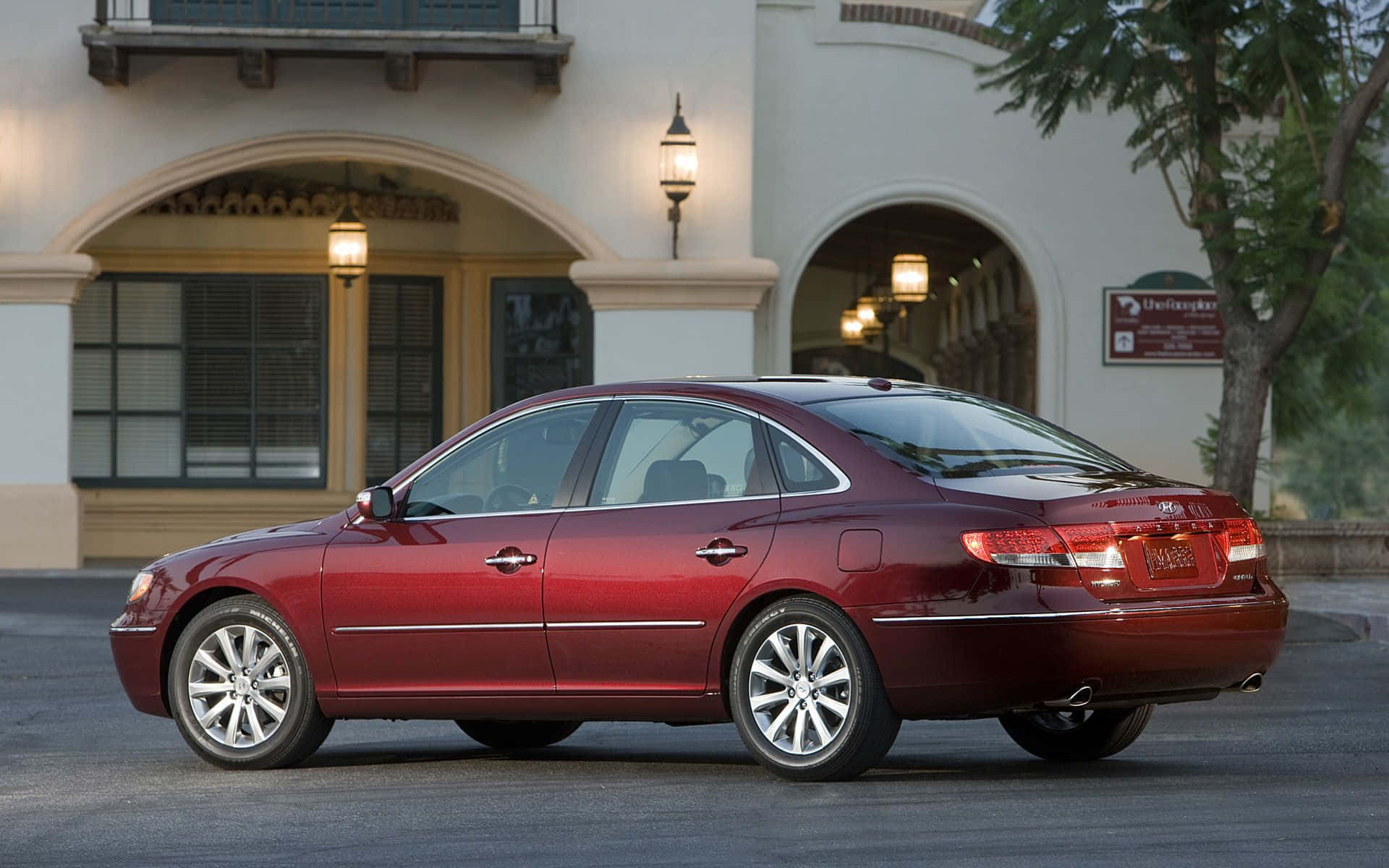 Hyundai Azera 桌布 壁紙 — 一輛光澤的栗色轎車停在一棟西班牙風格建築前，溫暖的燈籠燈光在黃昏中閃爍。