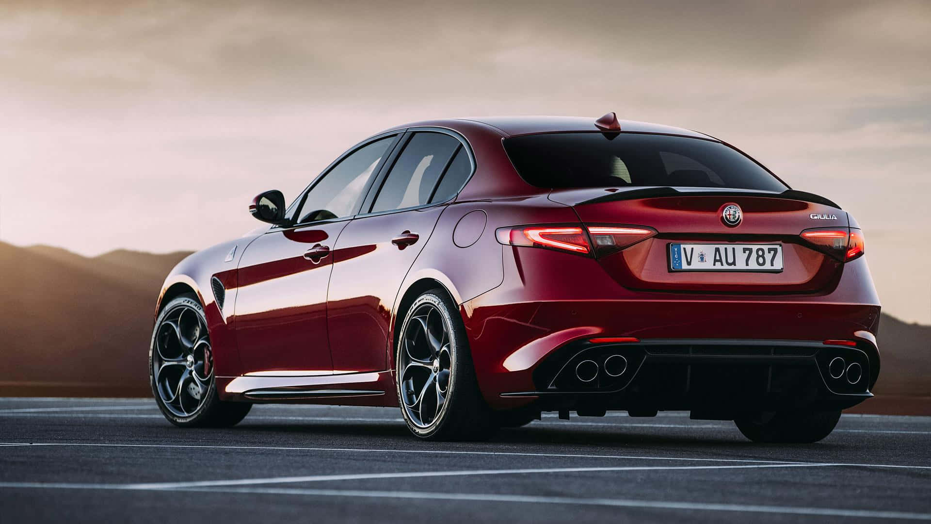 Alfa Romeo Giulia 桌布 壁紙 — 一輛光澤的紅色Alfa Romeo Giulia Quadrifoglio房車停在瀝青路上，背景是山脈，天空柔和夕陽。