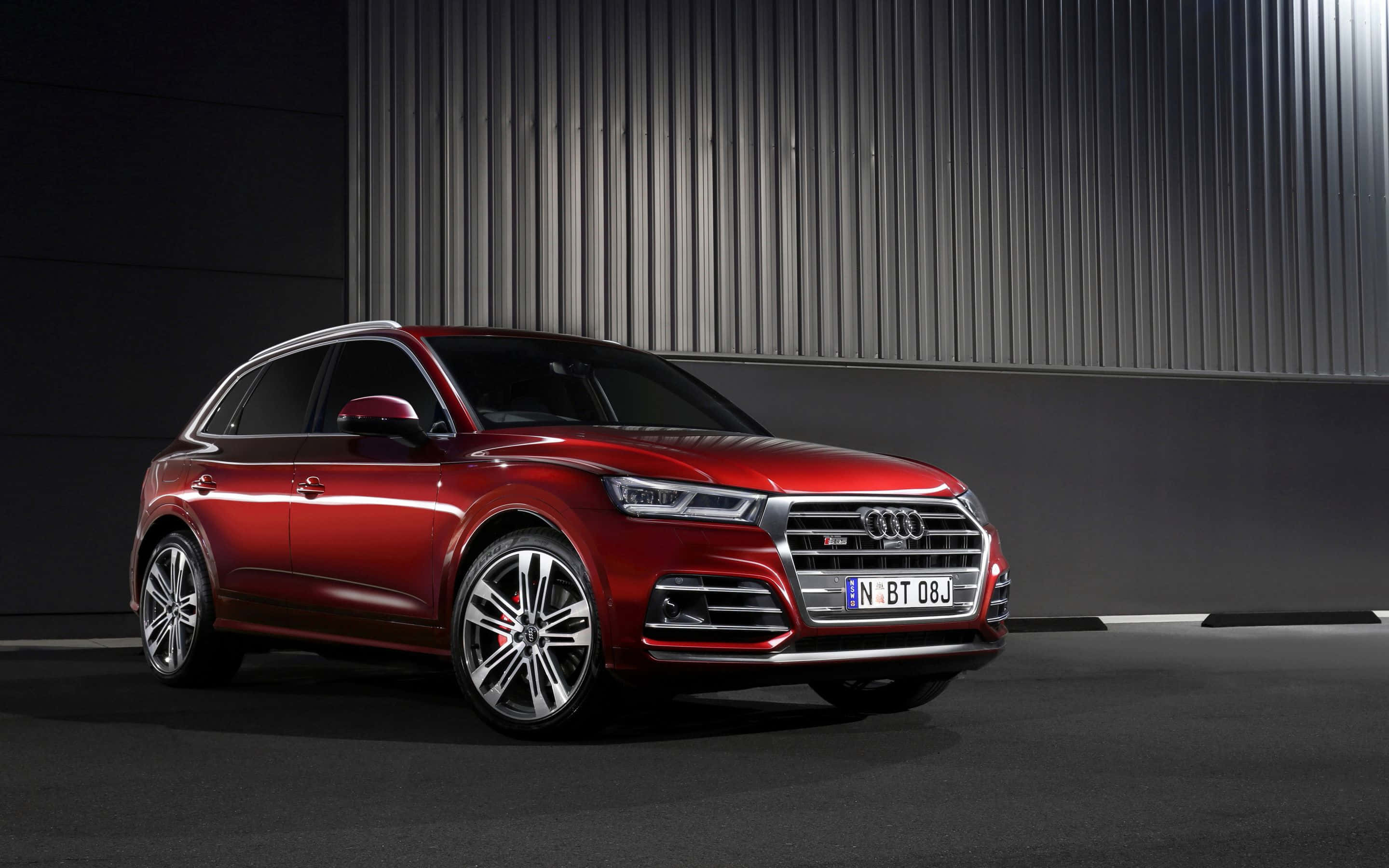 Audi Sq5 桌布 壁紙 — 一輛光澤的紅色Audi SQ5 SUV在時尚的工作室中展示，配有金屬牆壁和戲劇性燈光。