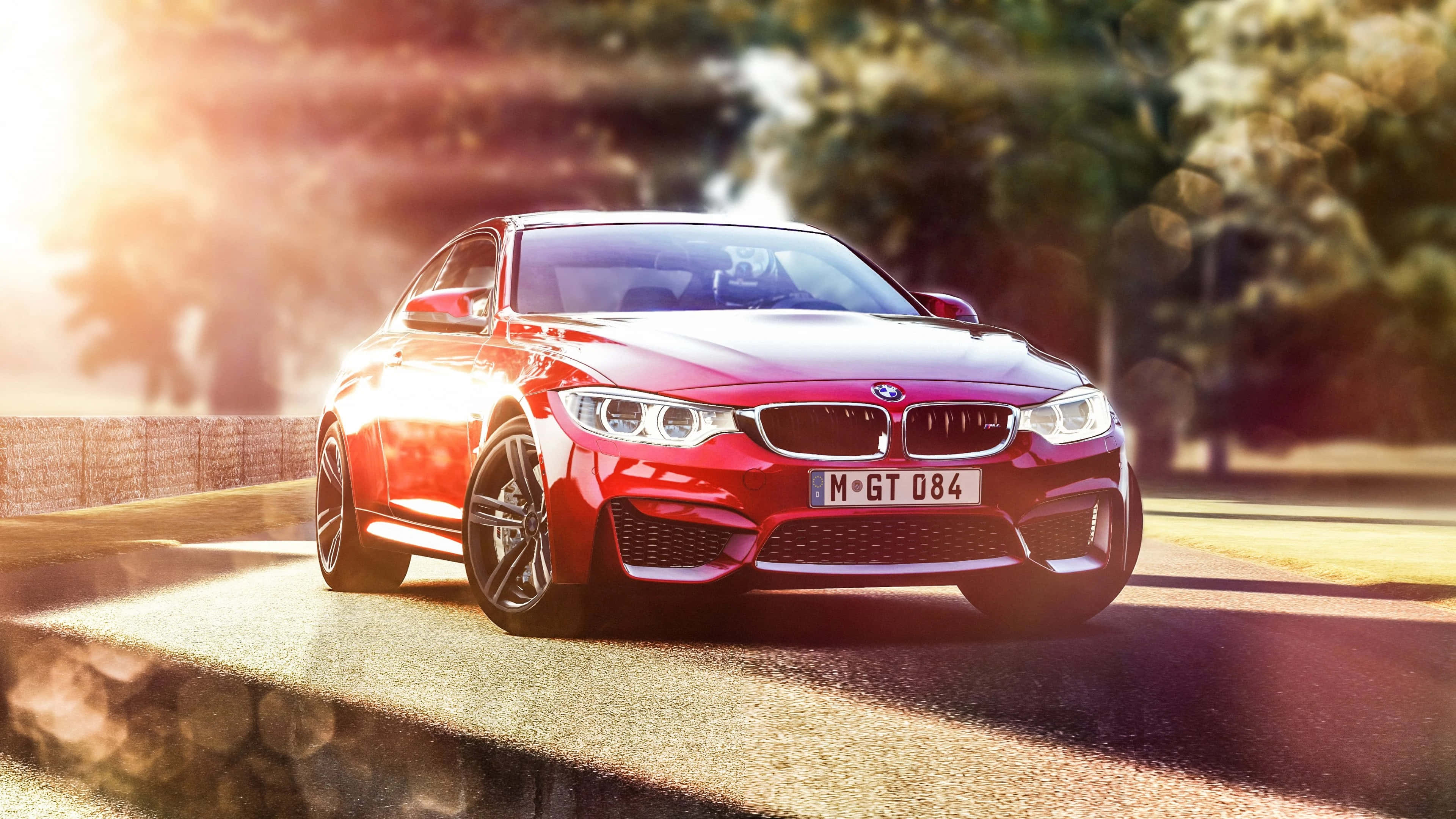 4K BMW 壁紙 桌布 壁紙 — 一輛光澤的紅色BMW M4 GT4跑車在陽光普照的賽道上疾馳，背景有模糊的樹木和溫暖的鏡頭光暈。