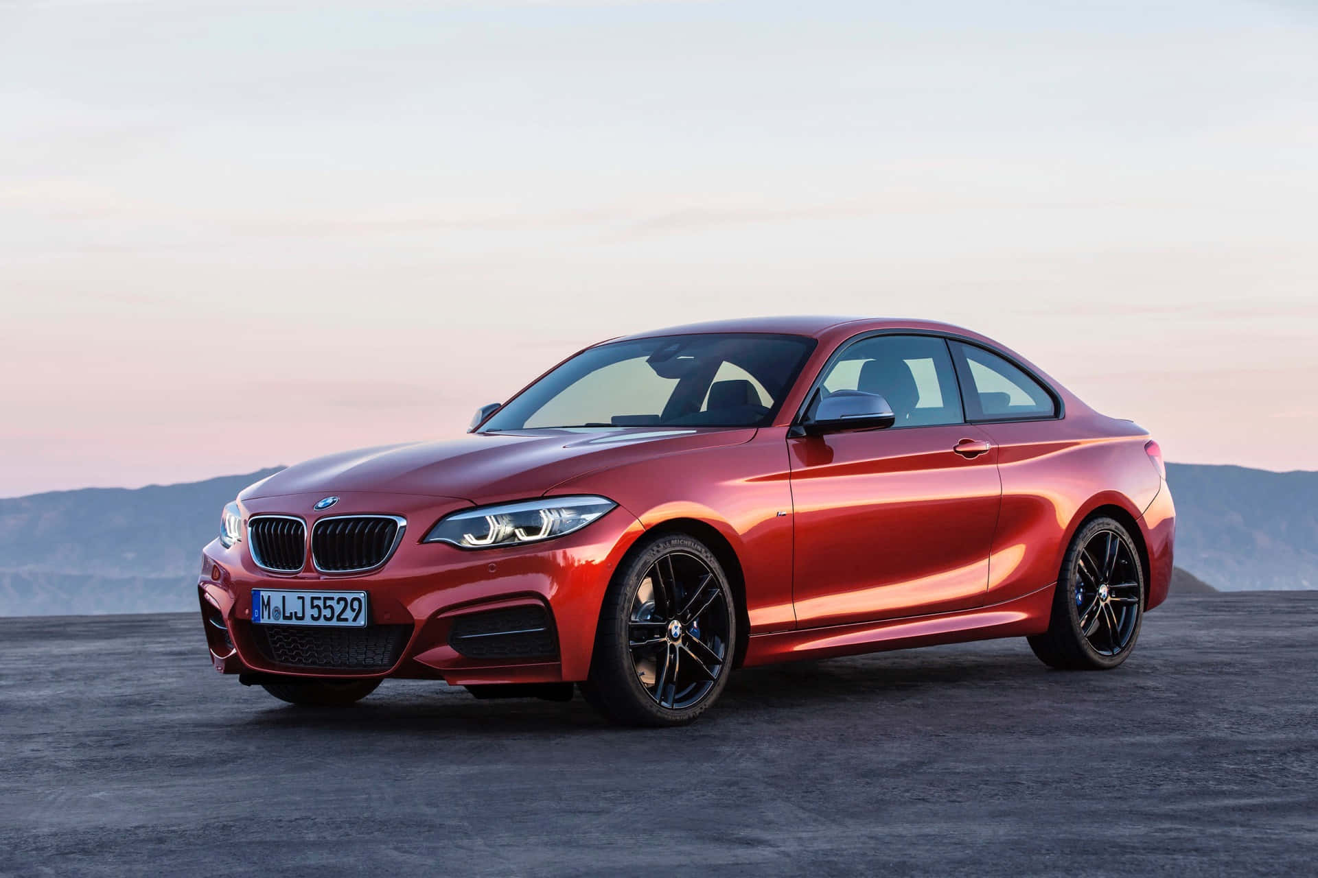 Bmw 2 Series 桌布 壁紙 — 一輛光澤的紅色BMW雙門跑車停在沙漠觀景點，背景是日落時分柔和的粉紅色和橙色天空。